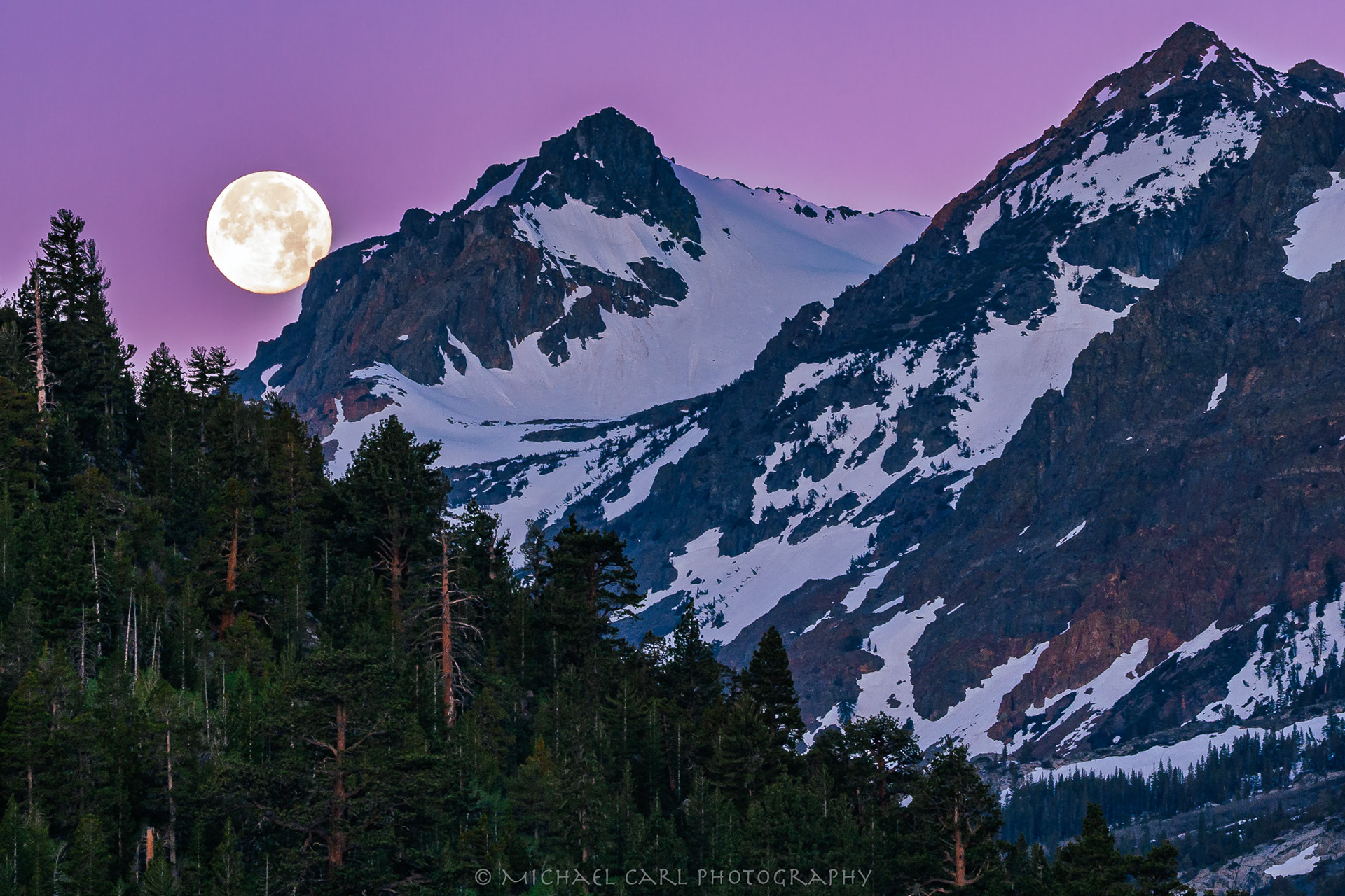 Sierra Nevada Mountains photography of full moon setting over snow covered peaks.