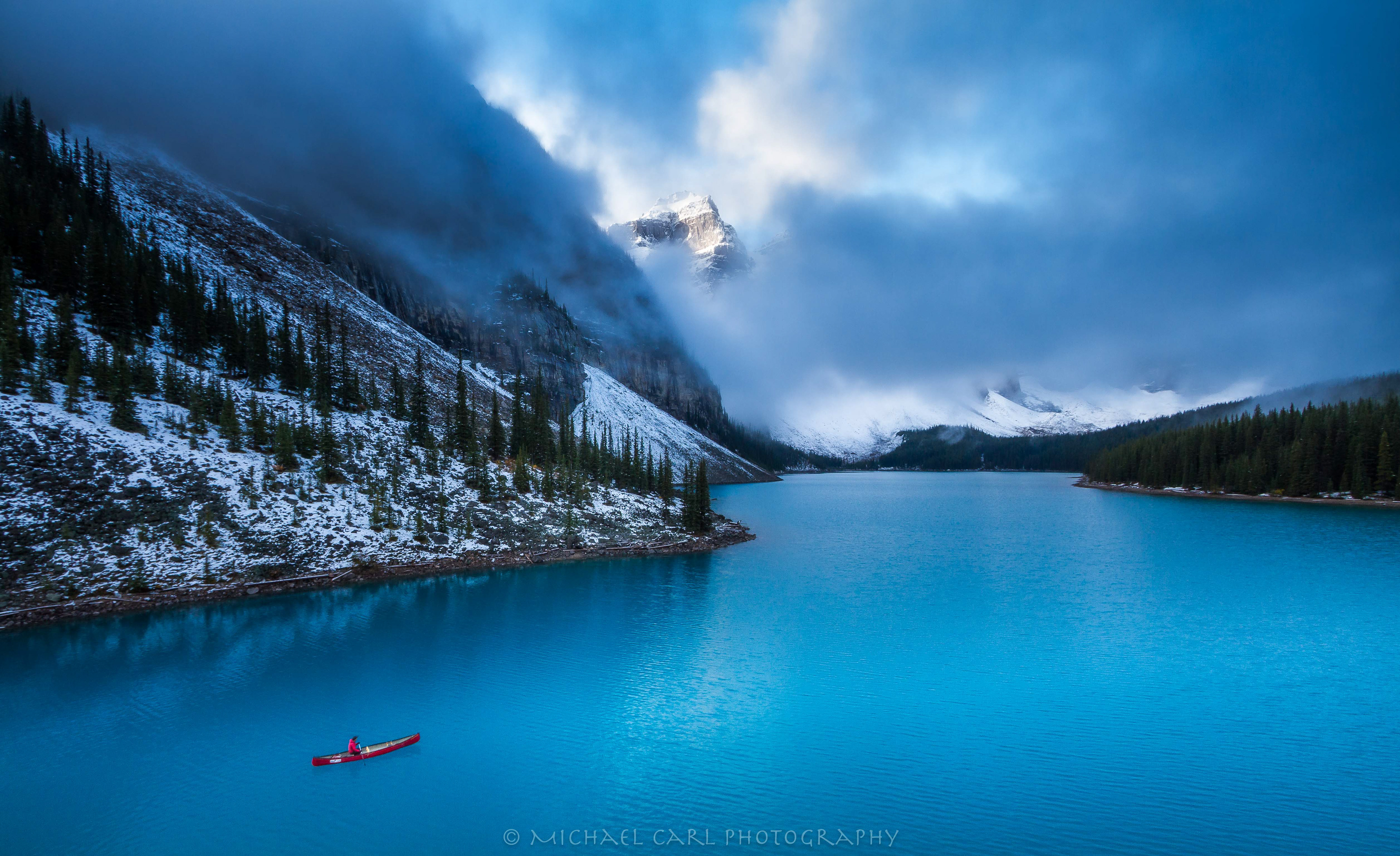 Landscape photography of mountain peak emerging from low clouds above Moraine Lake in Banff National Park Canada.