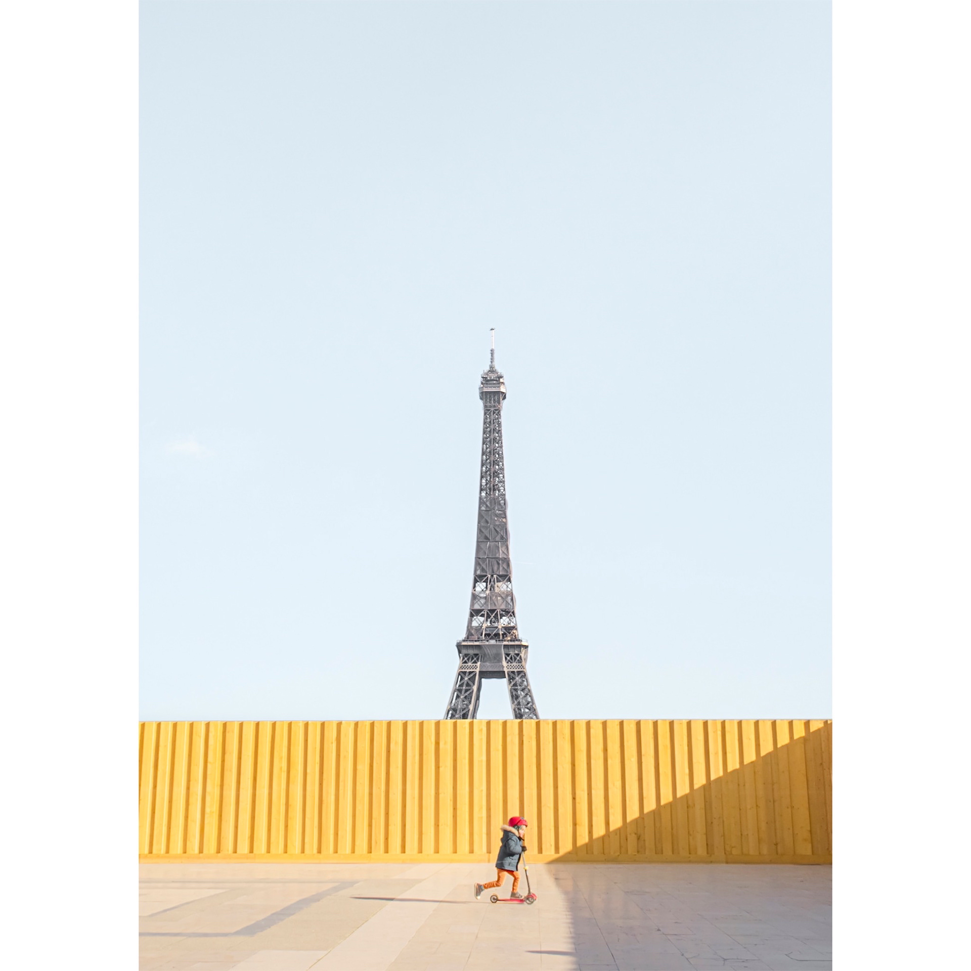 Minimal picture of a child in front of a colorful wall at Place du Trocadéro in Paris.The Eiffel Tower in the background and a soft blue sky