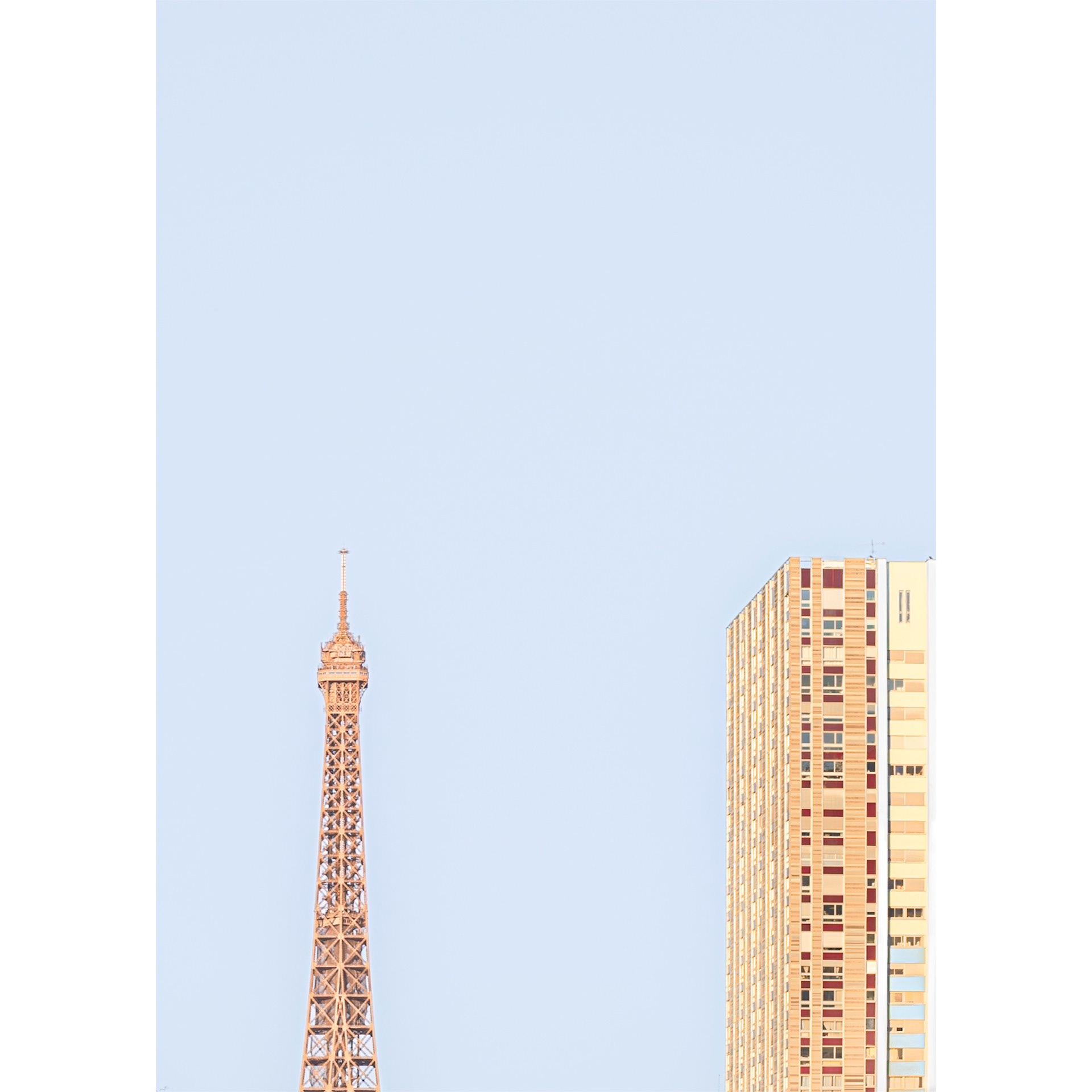 Top of the Eiffel Tower next to an office building and a large clear sky. Abstract and minimalist composition with soft colors.