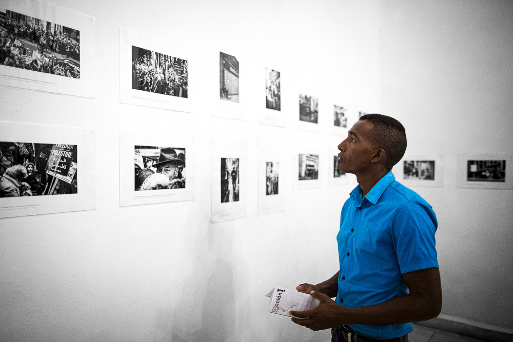 Picture of the frames on the exhibition wall with the caption and also Gallery Attendant at "londres. Detrás y debajo del palacio de buckingam" exhibition space. gallery arte soy in santiago de cuba, cuba. 2015 © Pedro Rodrigues