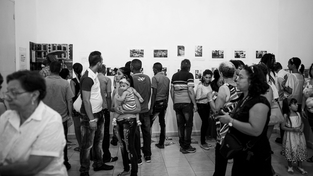 Picture of the frames on the exhibition wall with the caption and also many Gallery Attendants at "Londres. Detrás y debajo del palacio de buckingam" exhibition space. gallery arte soy in santiago de cuba, cuba. 2015 © Pedro Rodrigues