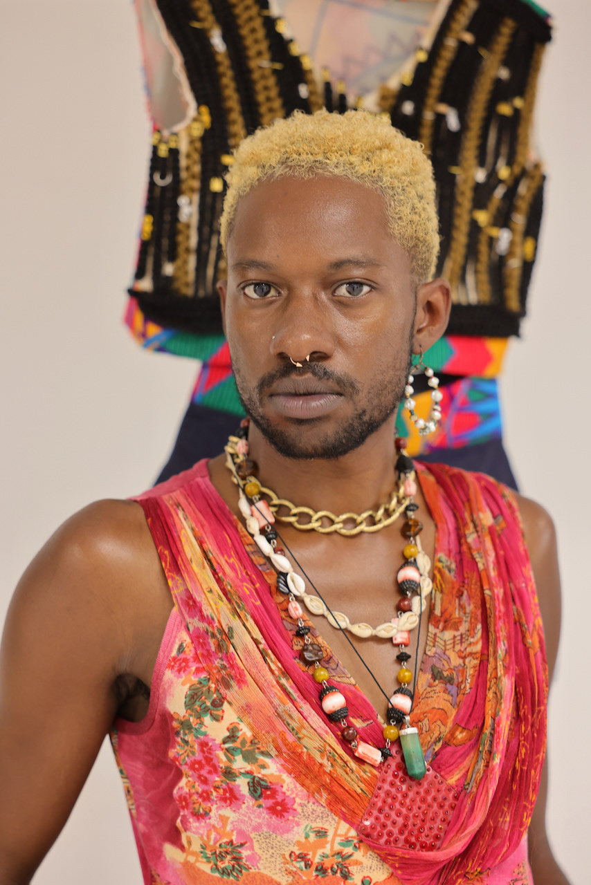 Kween Ramel Title: Roots For our hair to grow, we have to look after and nurture our roots. The collection “ROOTS” dissects the relationship we have with our hair and how our hair is a symbol of power and freedom. This collection expresses the powers and richness within our roots. The foundations that have been laid out for us. Within my research, I have explored the history of Afro hair and the discrimination and abuse black beings has received due to their hair. Black people have been told they are less than or not good enough because of their hair. Black people were treated like animals. Black people were told they were not attractive because of their hair. This collection opens us up to black people’s pain for us to accept our trauma and abuse to free ourselves. Reclaiming their royalty. Reclaiming their crown. “Roots” identifies the polarities in this human experience. Embracing the darkness to tap into the bright light within ourselves. This collection clashes aspect of black people’s history and their future, aligning the roots to where we are going too. Freedom. The use of Kente cloth and denim fabric displays our connection to our past and our future. “Roots” also plays with the polarities of genders and sexuality which is explored within this collection. I attained a lot of inspiration for the colours and silhouettes from West African traditional wear and also intertwining aspects of my Caribbean background. Cotton, wax fabric, synthetic hair, 2022