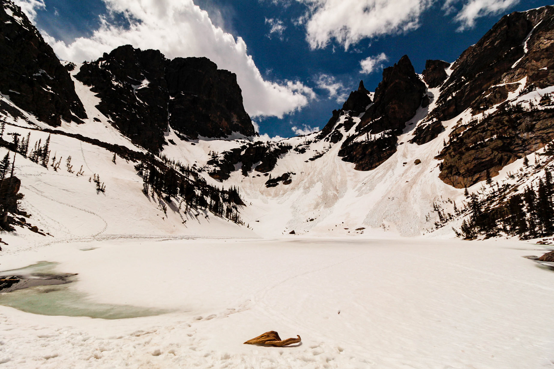 Photograph of Emerald Lake covered in snow in Rocky Mountain National Park, Colorado, with a frozen alpine lake, snow-lined shoreline, evergreen forest, and towering granite peaks.