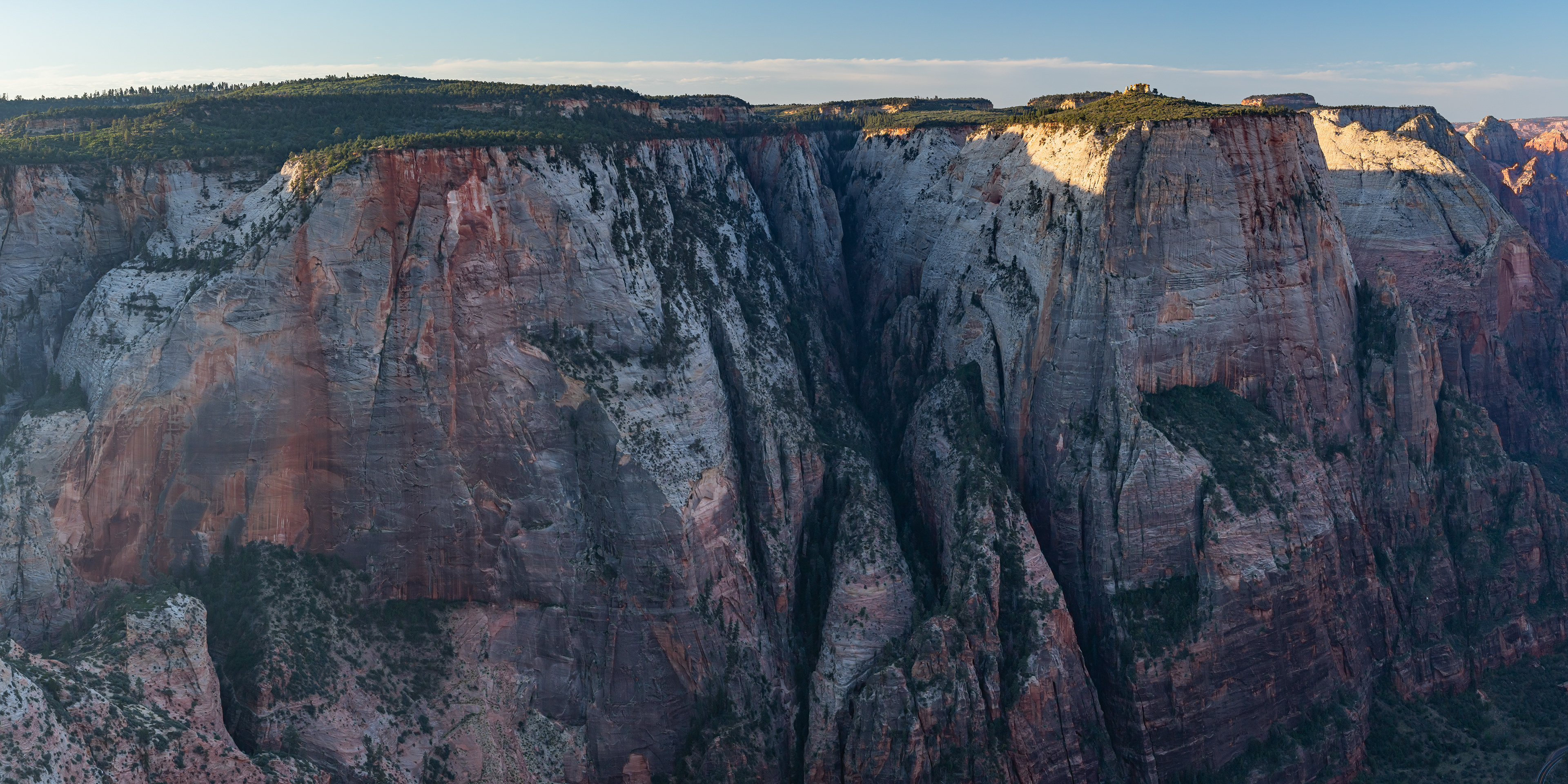 A sweeping view from Observation Point showing Zion Canyon far below, with sheer sandstone cliffs, layered mesas, and the Virgin River winding through the valley under a clear sky in Zion National Park.