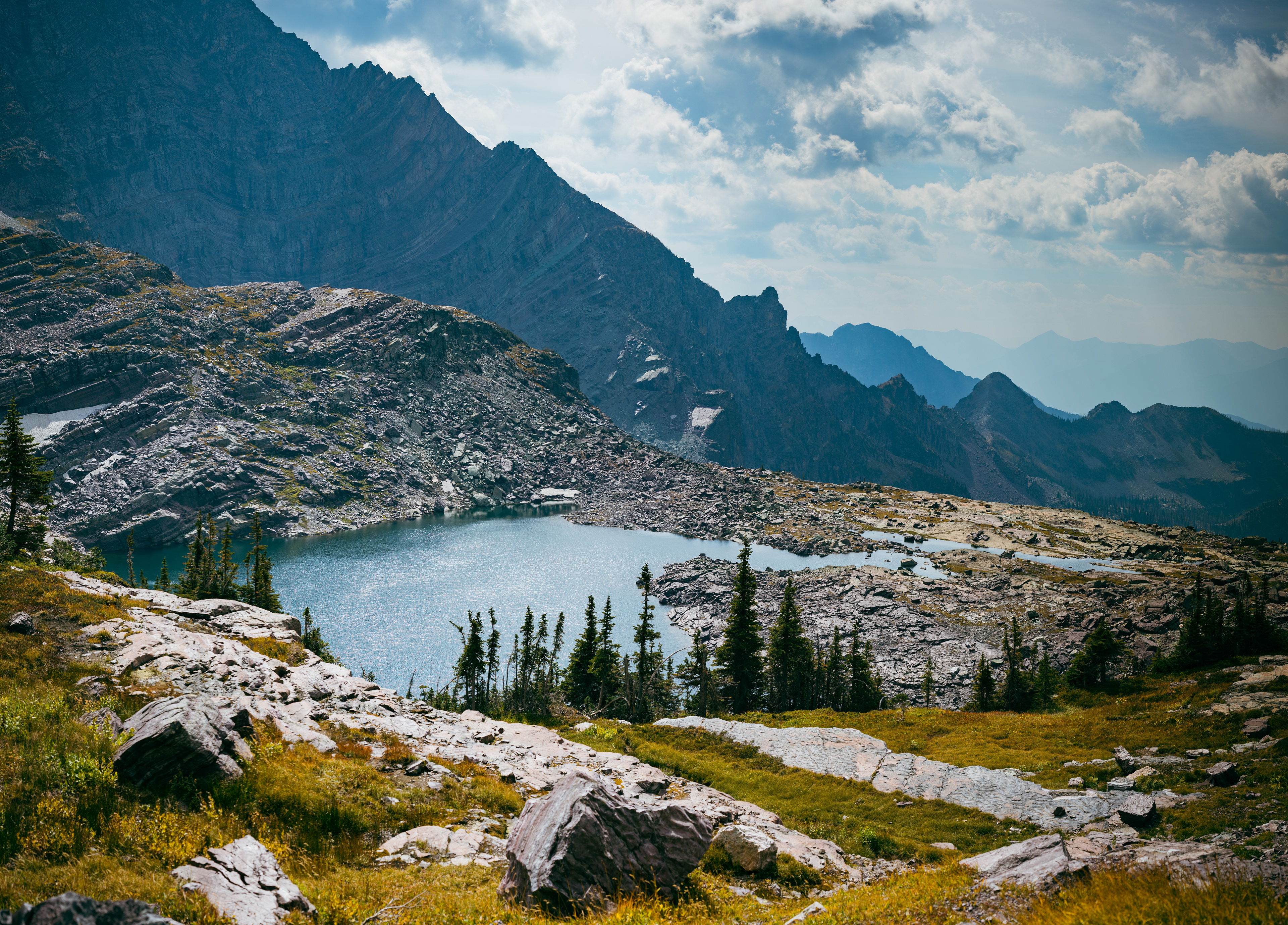 Landscape photograph of Feather Woman Lake in Glacier National Park, Montana, featuring a remote alpine lake, evergreen forest, and rugged peaks.