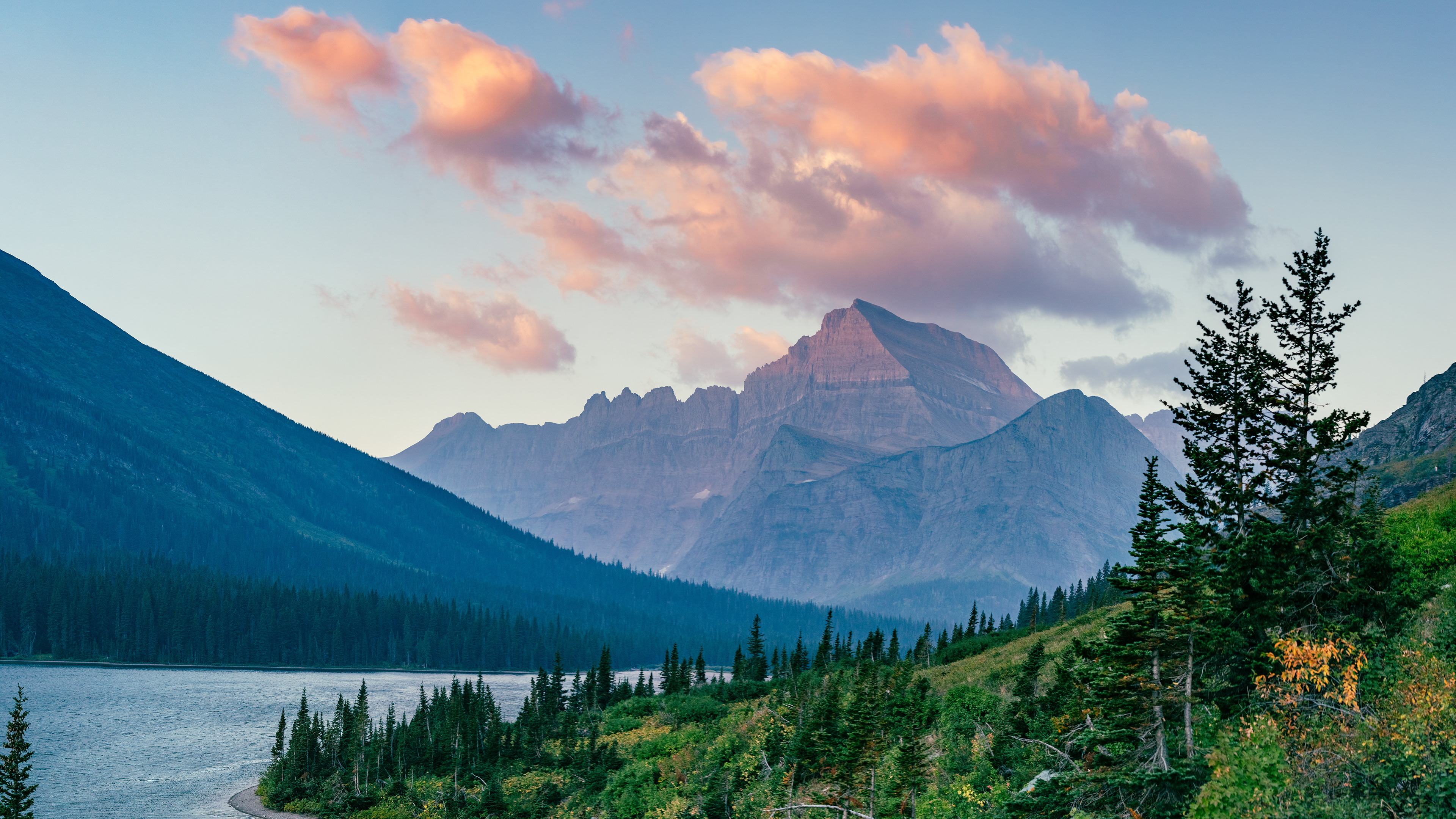 Photograph of Little Chief Mountain rising above St. Mary Lake in Glacier National Park, Montana, with forested shoreline, alpine peaks, and colorful evening clouds over the mountains.