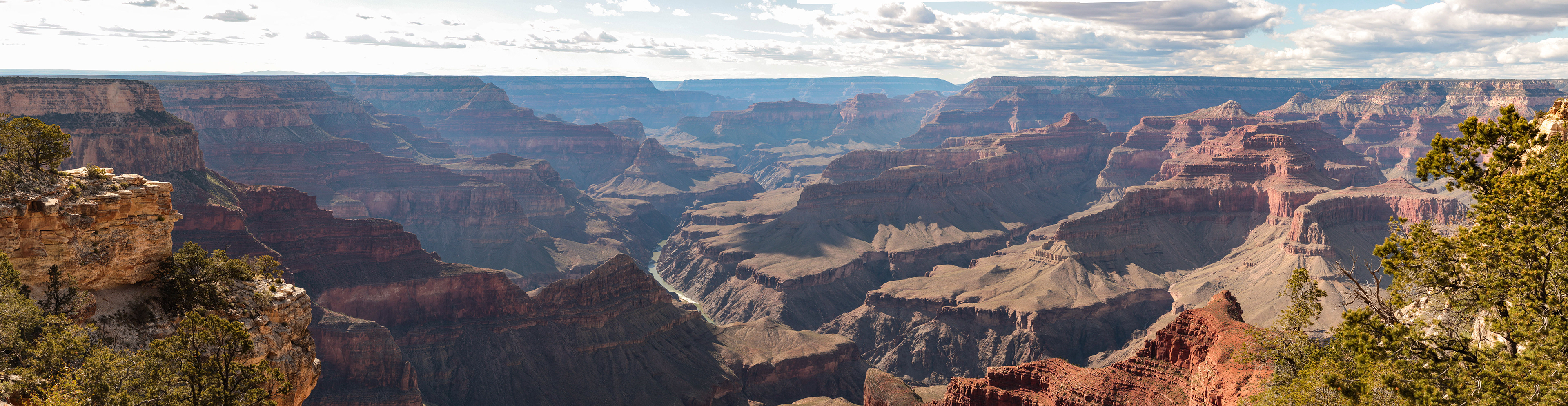 Photograph of a sweeping view of the Grand Canyon, with layered red rock formations, deep canyon walls, and the Colorado River winding through the canyon floor.