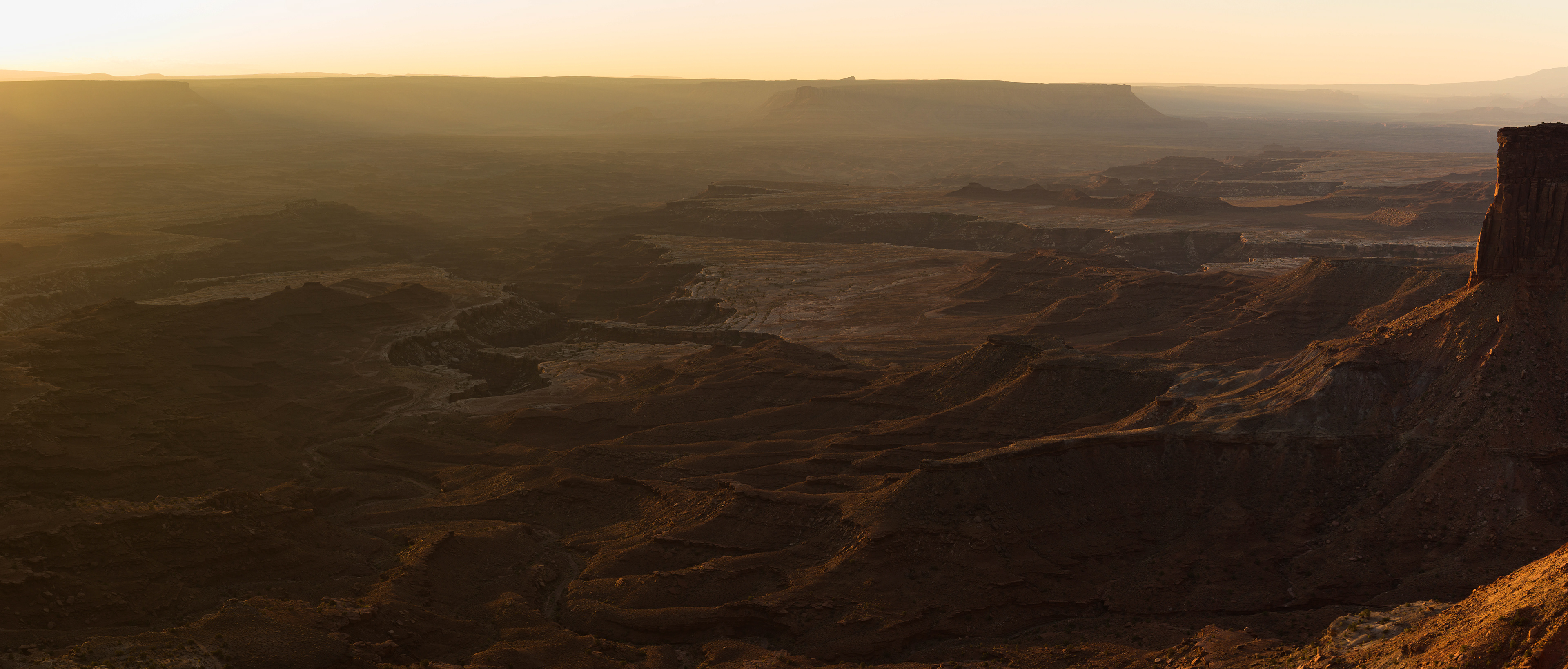 Photograph of Canyonlands National Park at sunset in Utah, with warm evening light illuminating layered canyons and expansive desert terrain.