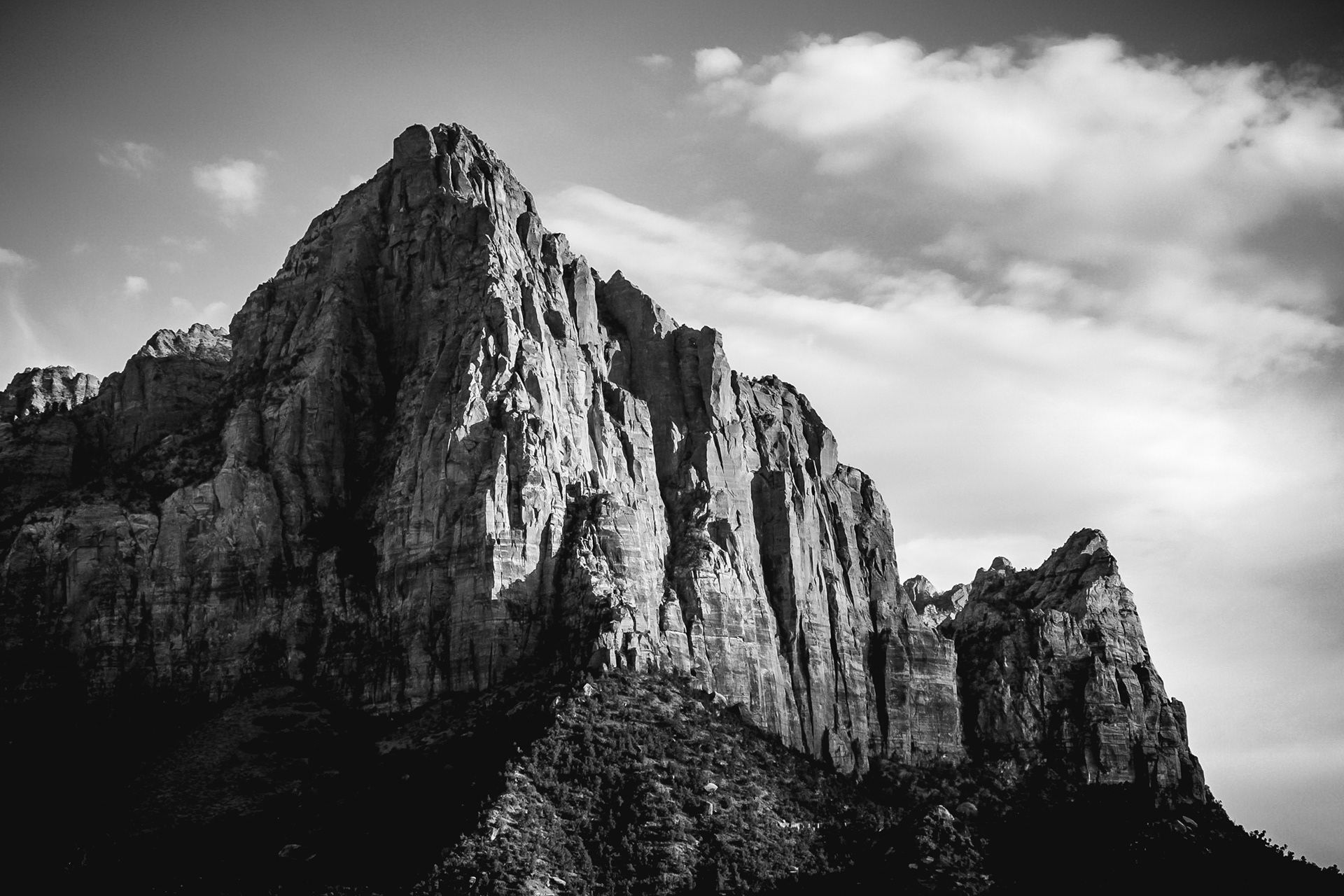 Black and white photograph of The Watchman in Zion National Park, Utah, featuring dramatic sandstone cliffs, desert vegetation, and strong tonal contrast.
