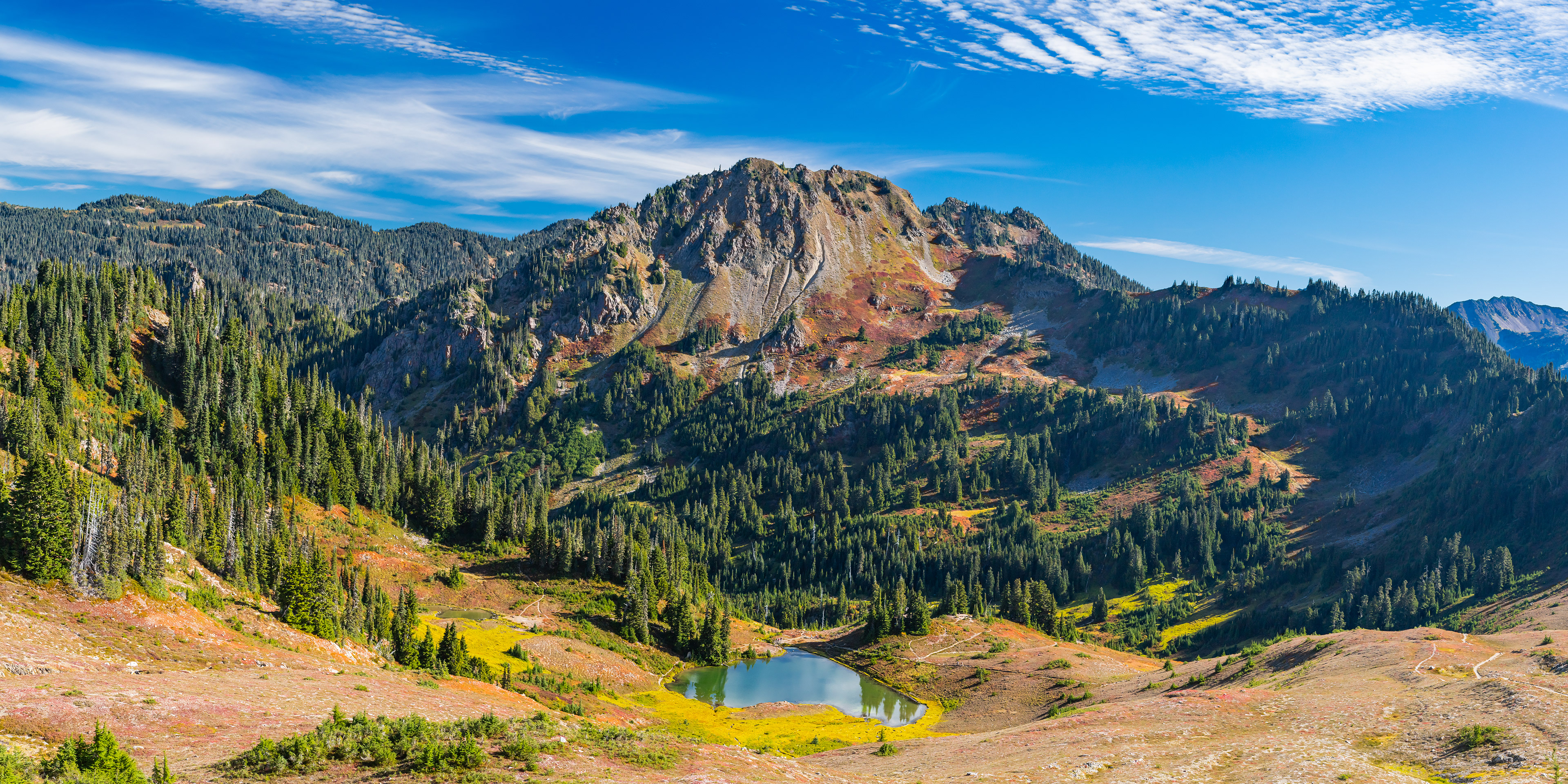 Photograph of Heart Lake in Olympic National Park, Washington, with calm alpine water and mountains rising in the background.