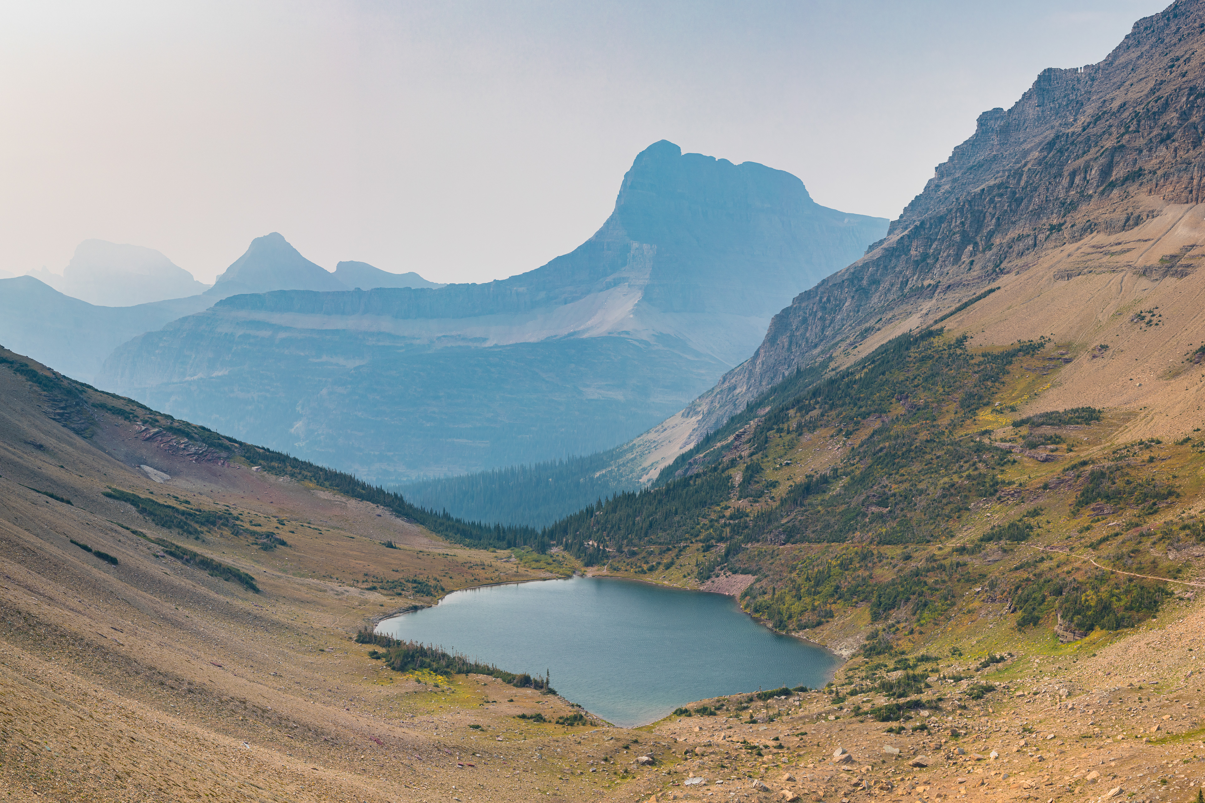 Photograph of Ptarmigan Lake in Glacier National Park on a smoky day, with muted light and surrounding alpine terrain