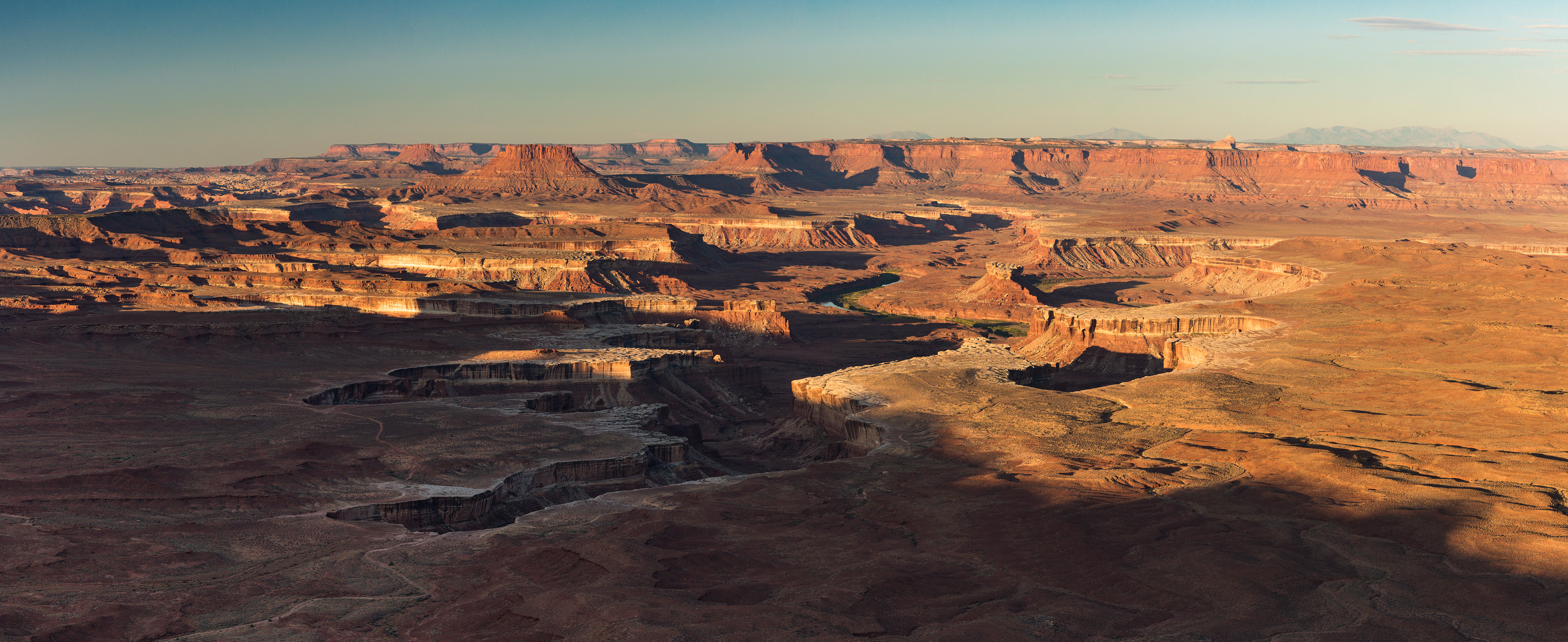 Photograph of Canyonlands National Park at golden hour in Utah, with warm light highlighting layered canyons, mesas, and expansive desert terrain.