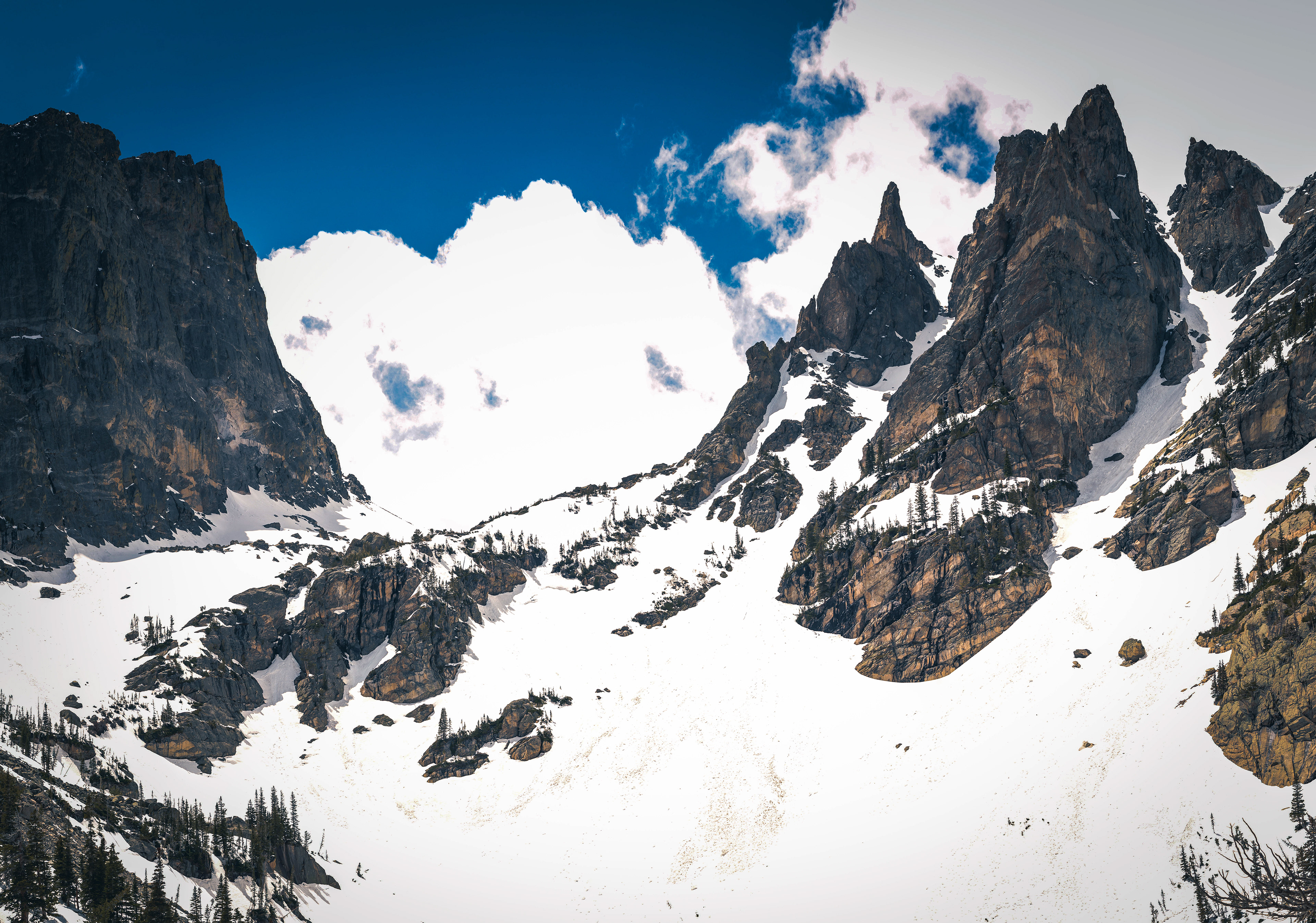 Photograph of Emerald Lake covered in snow in Rocky Mountain National Park, Colorado, with a frozen alpine lake, snow-lined shoreline, evergreen forest, and towering granite peaks.