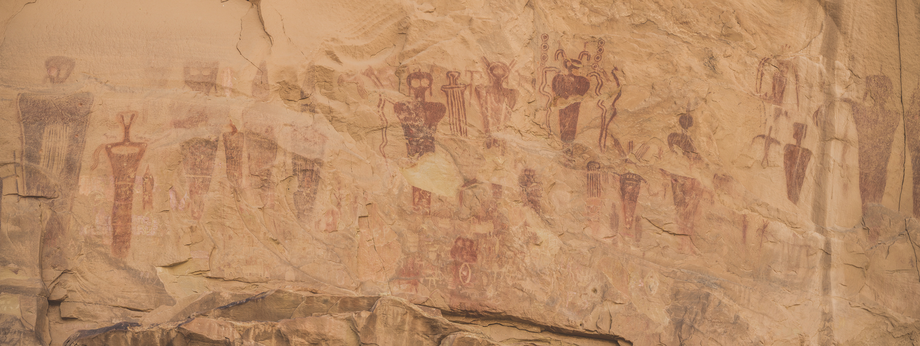 Photograph of ancient rock art petroglyphs on a sandstone wall in Canyonlands National Park, Utah, showing human figures and symbolic designs painted onto the cliff face.