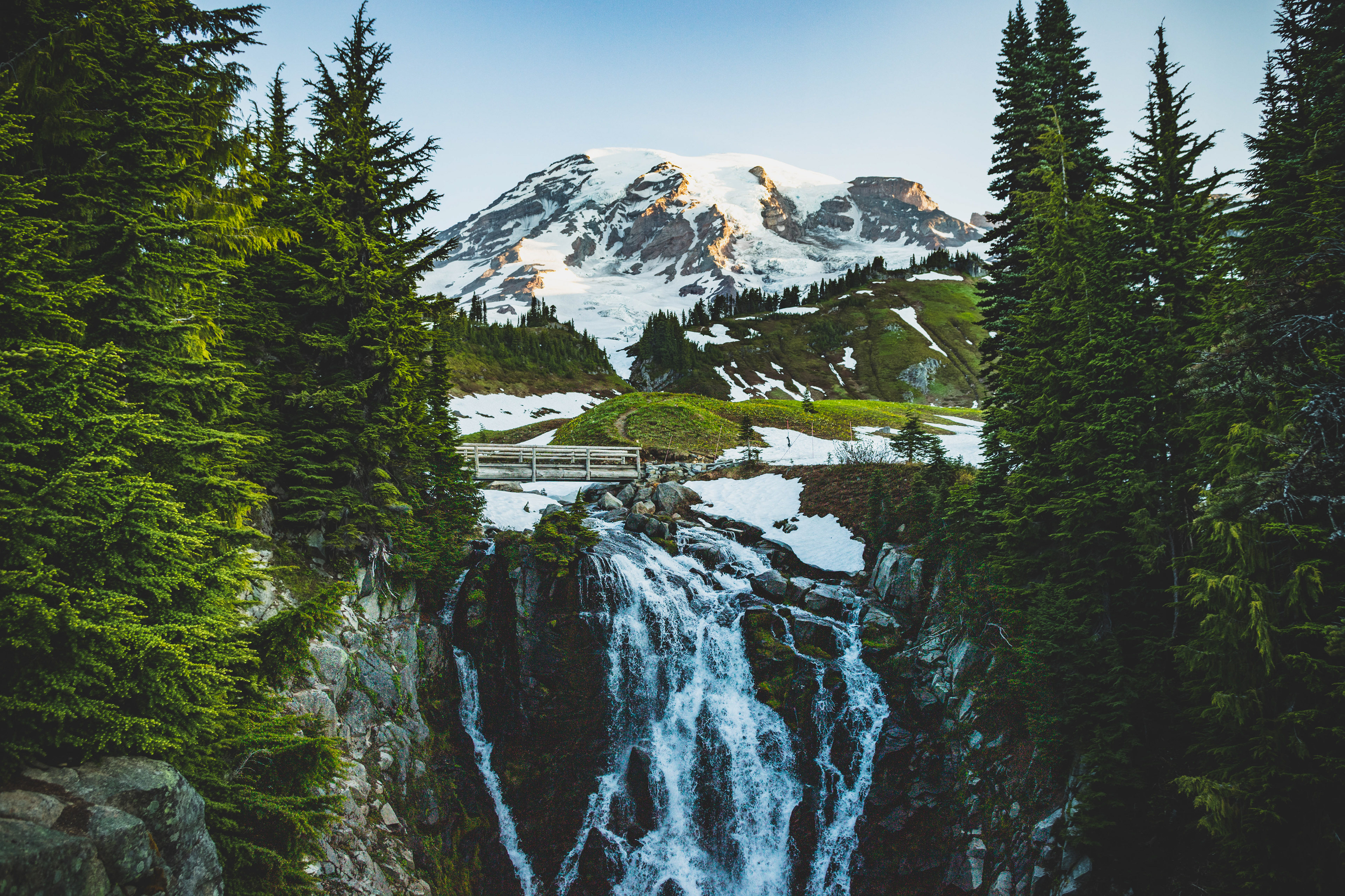 Photograph of Myrtle Falls with Mount Rainier in Mount Rainier National Park, Washington, featuring cascading water, wildflower-lined cliffs, and a snow-covered volcanic peak.