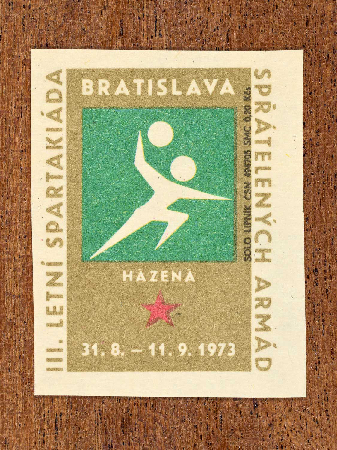 Vintage 1973 Czech matchbox label showing a simplified white handball player on a green and gold background. Produced by the Solo Lipník match factory to promote physical training and demonstrate collective military readiness among allied armies.