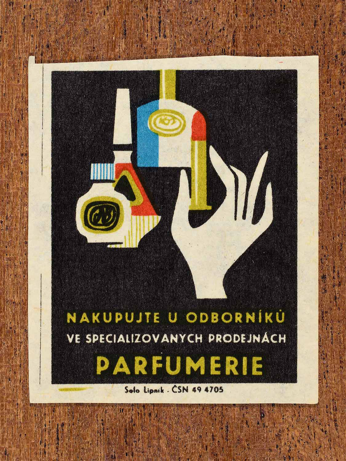 Vintage c. 1967 Czech matchbox label showing perfume and cosmetic products beside a stylised hand in black, yellow, red and blue colours. Produced by the Solo Lipník match factory to promote shopping for perfumes and cosmetics in specialised retail stores.