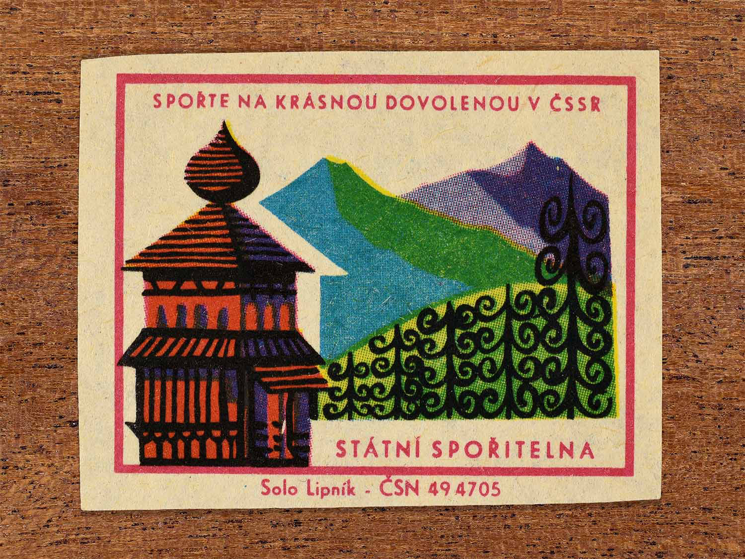 Vintage 1968 Czech matchbox label showing a traditional wooden folk building against a stylised mountain landscape. Produced by the Solo Lipník match factory to promote saving money for holidays in the Czechoslovak Socialist Republic.