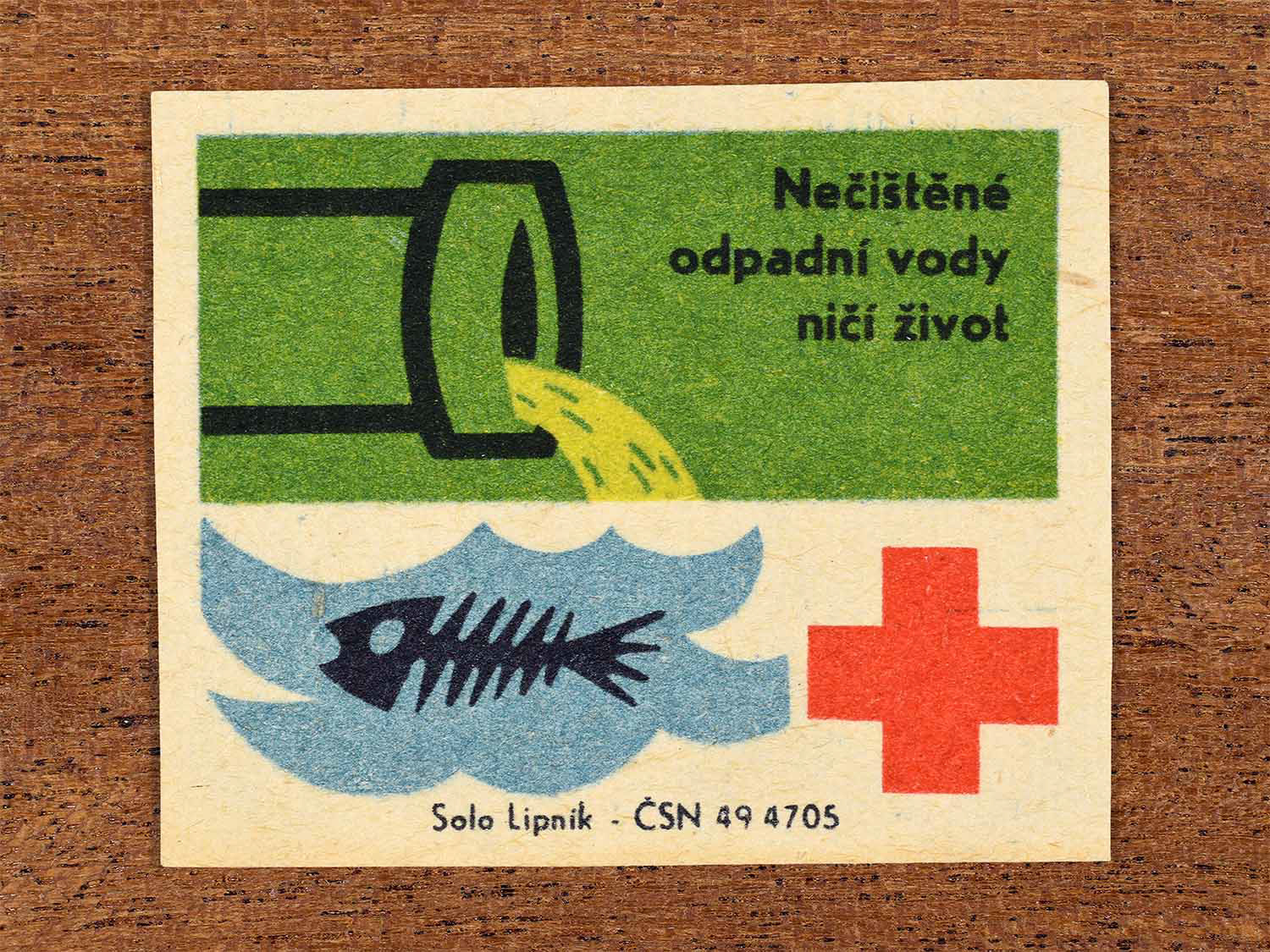 Vintage 1966 Czech matchbox label showing a pipe discharging waste above a fish skeleton with a red plus symbol in green and blue colours. Produced by the Solo Lipník match factory to warn that untreated wastewater destroys life.