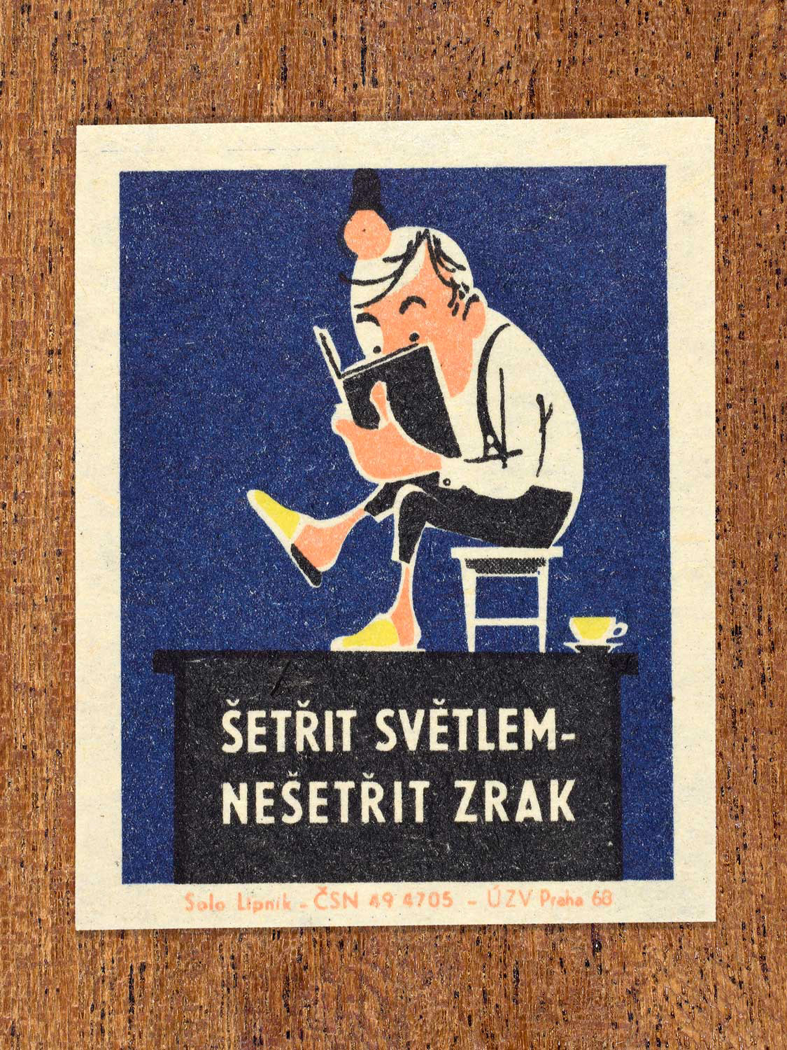 Vintage 1968 Czech matchbox label featuring a cartoon person sitting on a chair looking closely at a book with a hanging bulb above, on blue background. Produced by Solo Lipník match factory to promote proper lighting and maintenance for eye health and safe work practices.