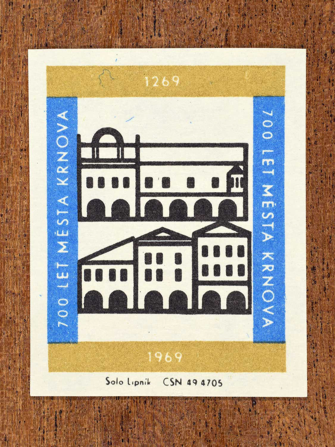 Vintage 1969 Czech matchbox label showing stylised historic burgess houses of Krnov in black with blue and gold framing. Produced by the Solo Lipník match factory to commemorate 700 years of the city of Krnov.