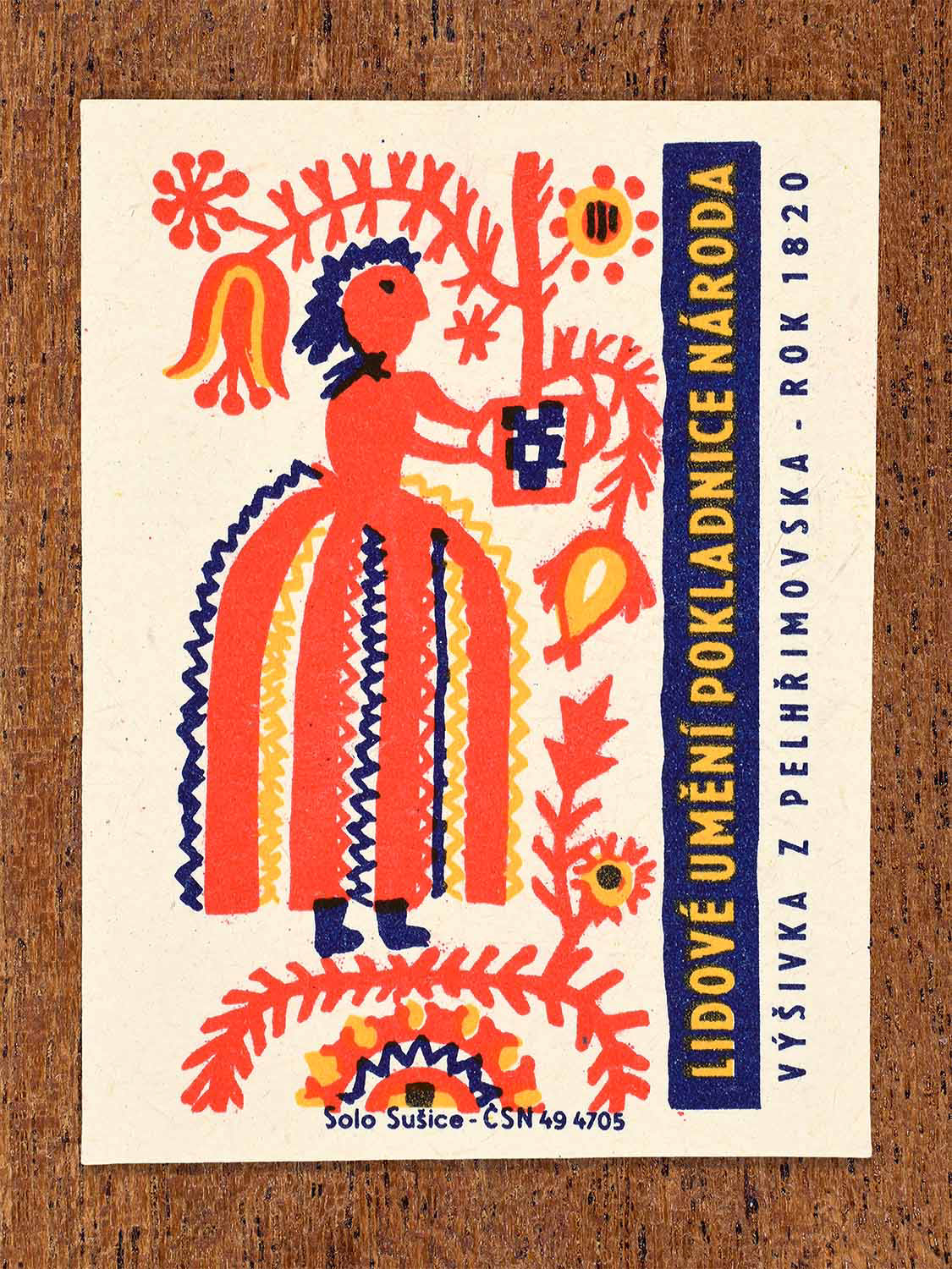 Vintage 1964 Czech matchbox label showing a stylised female folk figure in a wide embroidered skirt with floral motifs. Produced by the Solo Sušice match factory to depict embroidery from the Pelhřimov region.