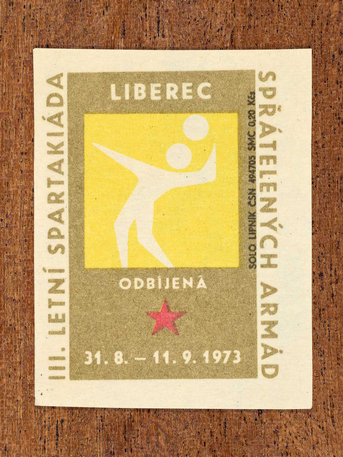 Vintage 1973 Czech matchbox label showing a simplified white volleyball player on a yellow and gold background. Produced by the Solo Lipník match factory to promote physical training and demonstrate collective military readiness among allied armies.