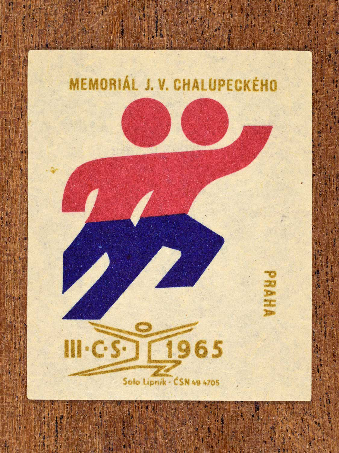 Vintage 1965 Czechoslovak matchbox label showing two stylised athlete figures. In blue, red and gold colours. Produced by the Solo Lipník match factory as a memorial to an athlete.