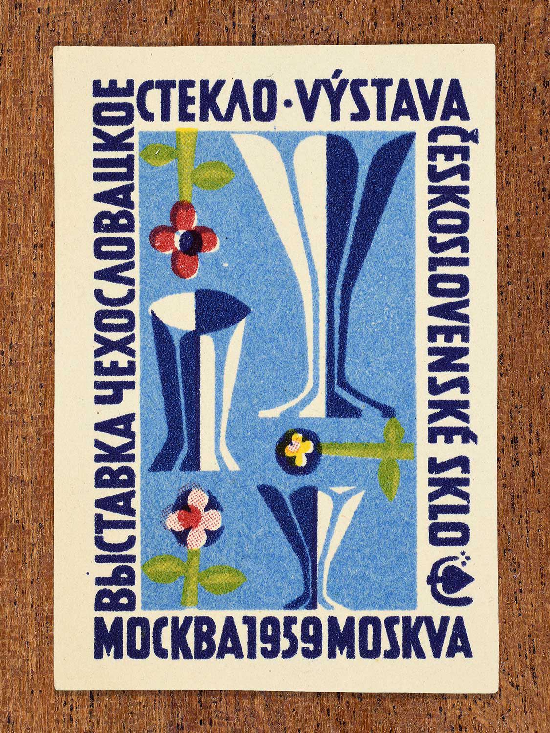 Mid-century modern Eastern Bloc illustration on a 1959 Czechoslovak matchbox label featuring three glass vessels on a dark blue background. Designed to promote an international glass exhibition in Moscow by an unknown factory.
