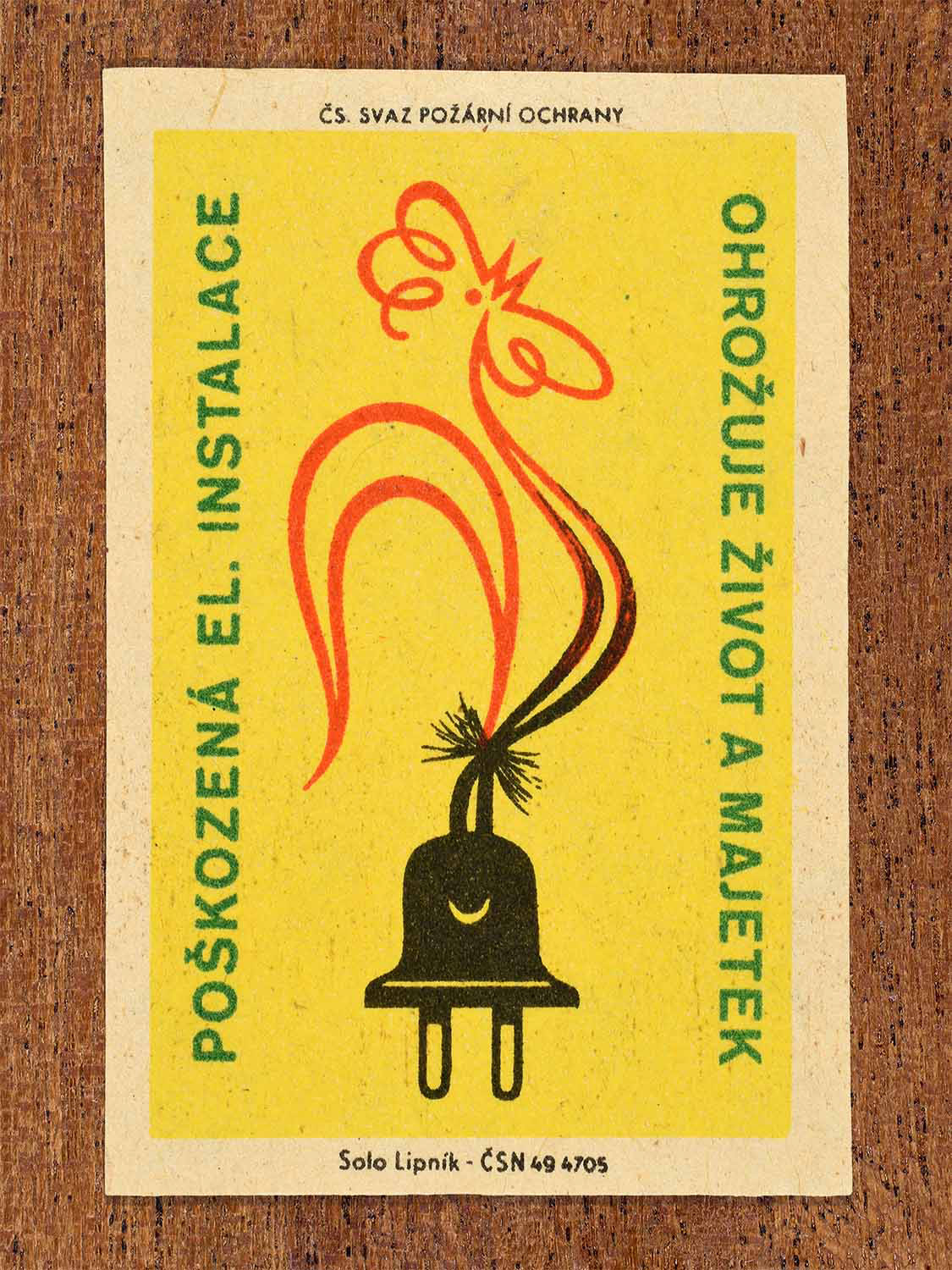 Vintage c. 1961 Czech matchbox label showing a damaged electrical plug with sparks forming a rooster in yellow and black colours. Produced by the Solo Lipník match factory to warn that faulty electrical installations endanger life and property.