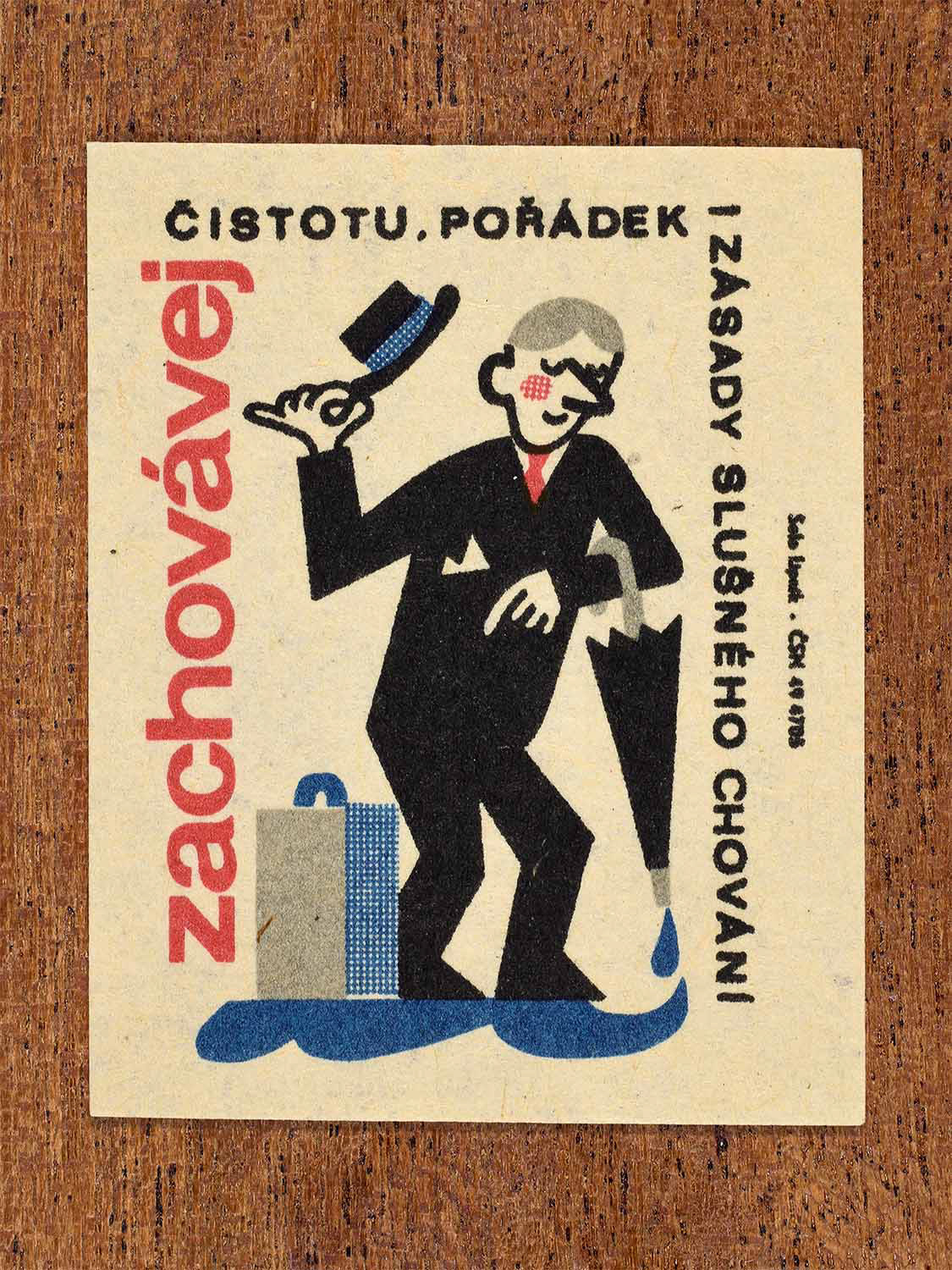 Vintage c. 1964 Czech matchbox label showing a man wearing a suit and holding an umbrella dripping with water. illustrated in black, blue and red. Produced by the Solo Lipník match factory to promote cleanliness, order, and proper public behaviour.