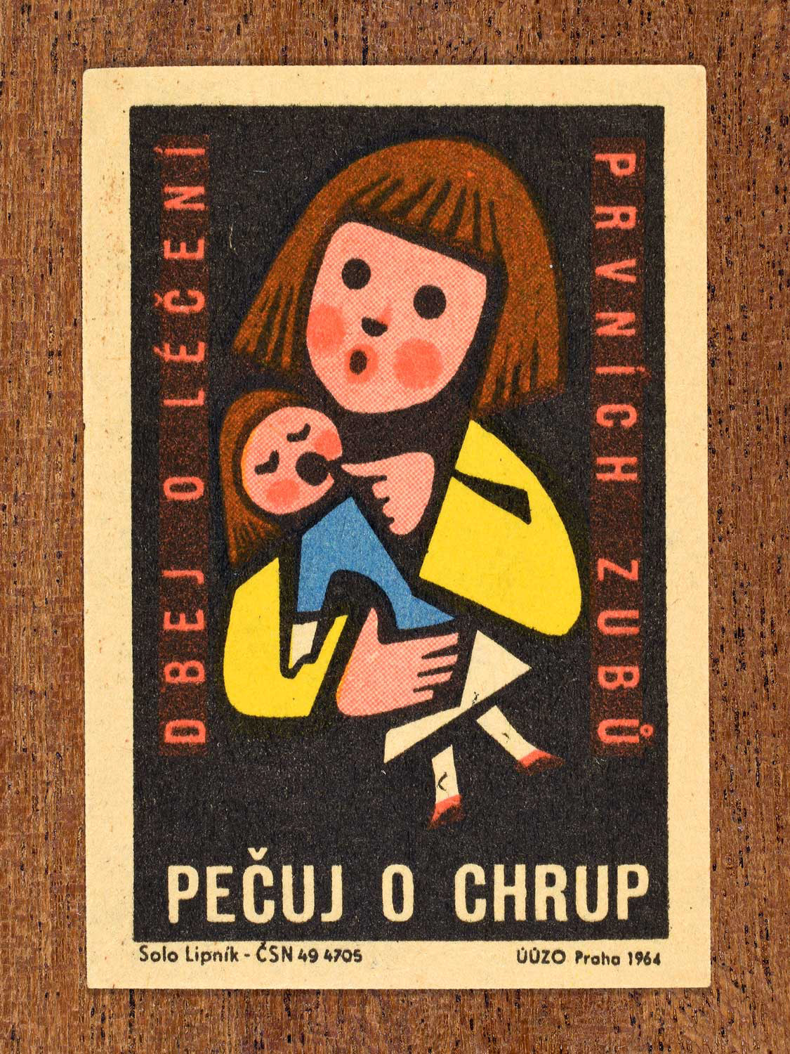 Vintage 1964 Czech matchbox label showing an illustrated child holding a doll and pointing at its mouth, on a black background. Produced by the Solo Lipník match factory to promote nutrition advice and hygiene habits in protecting healthy teeth.