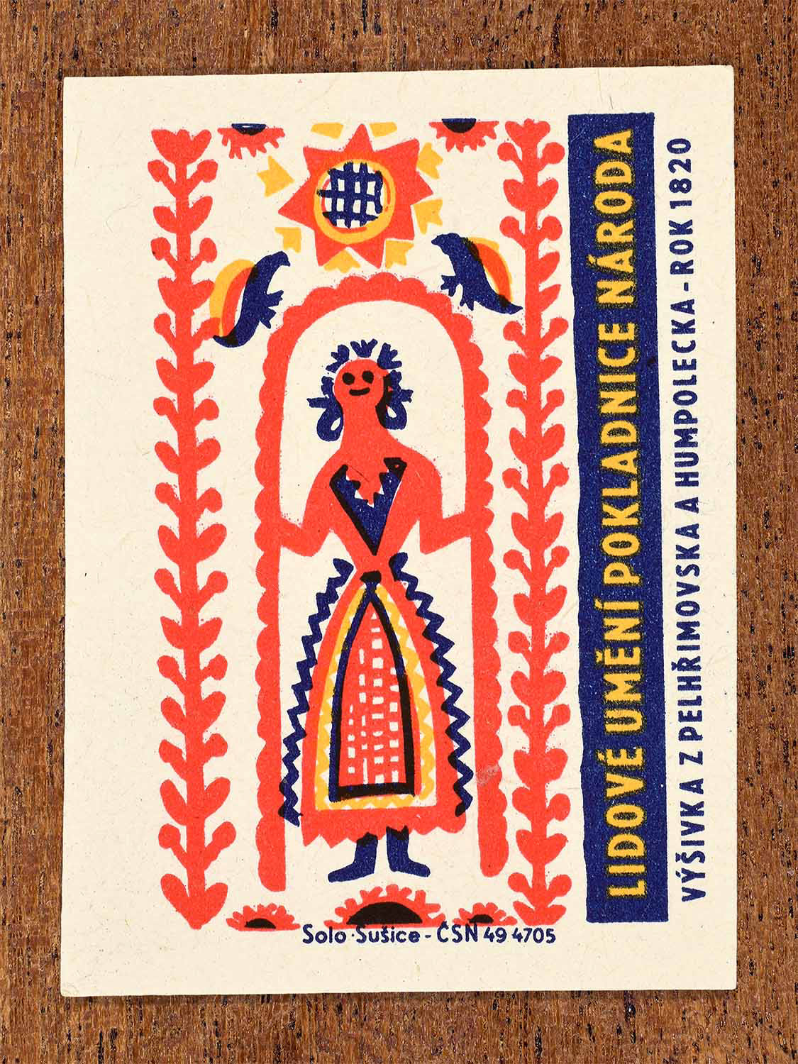 Vintage 1964 Czech matchbox label showing a stylised female folk figure with birds and floral borders in red, yellow and blue. Produced by the Solo Sušice match factory to feature Pelhřimov embroidery traditions.