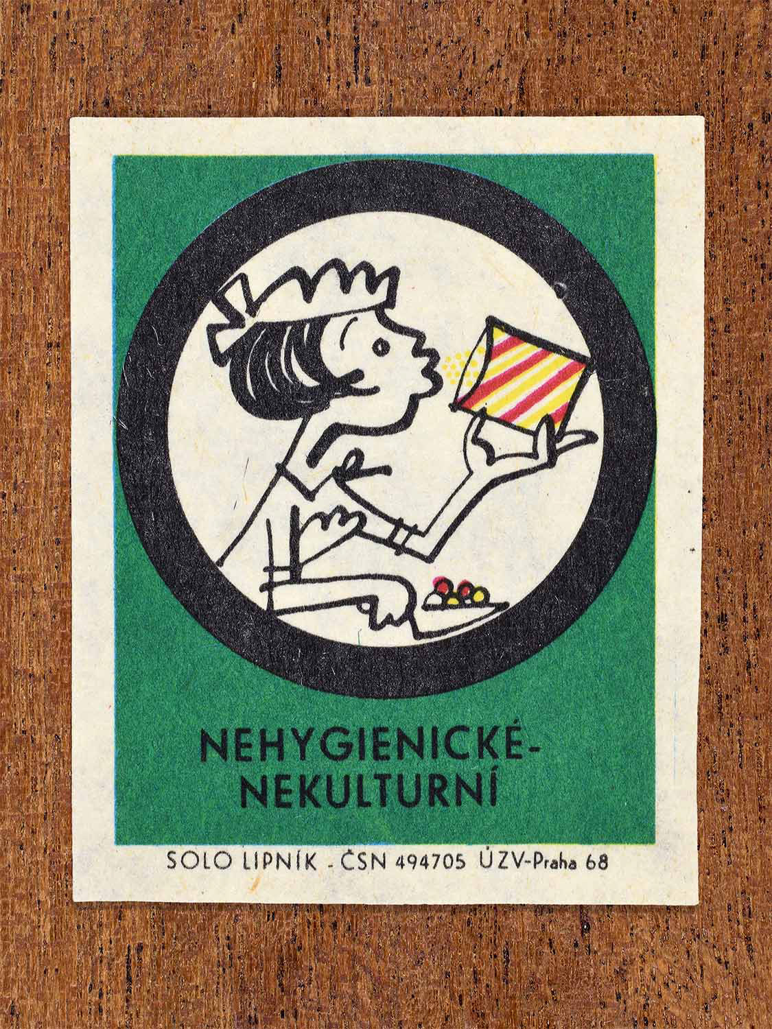 Vintage c. 1968 Czech matchbox label showing a person eating directly from packaging framed in a circle, on green background. Produced by the Solo Lipník match factory to discourage unhygienic and uncultured eating behaviour.