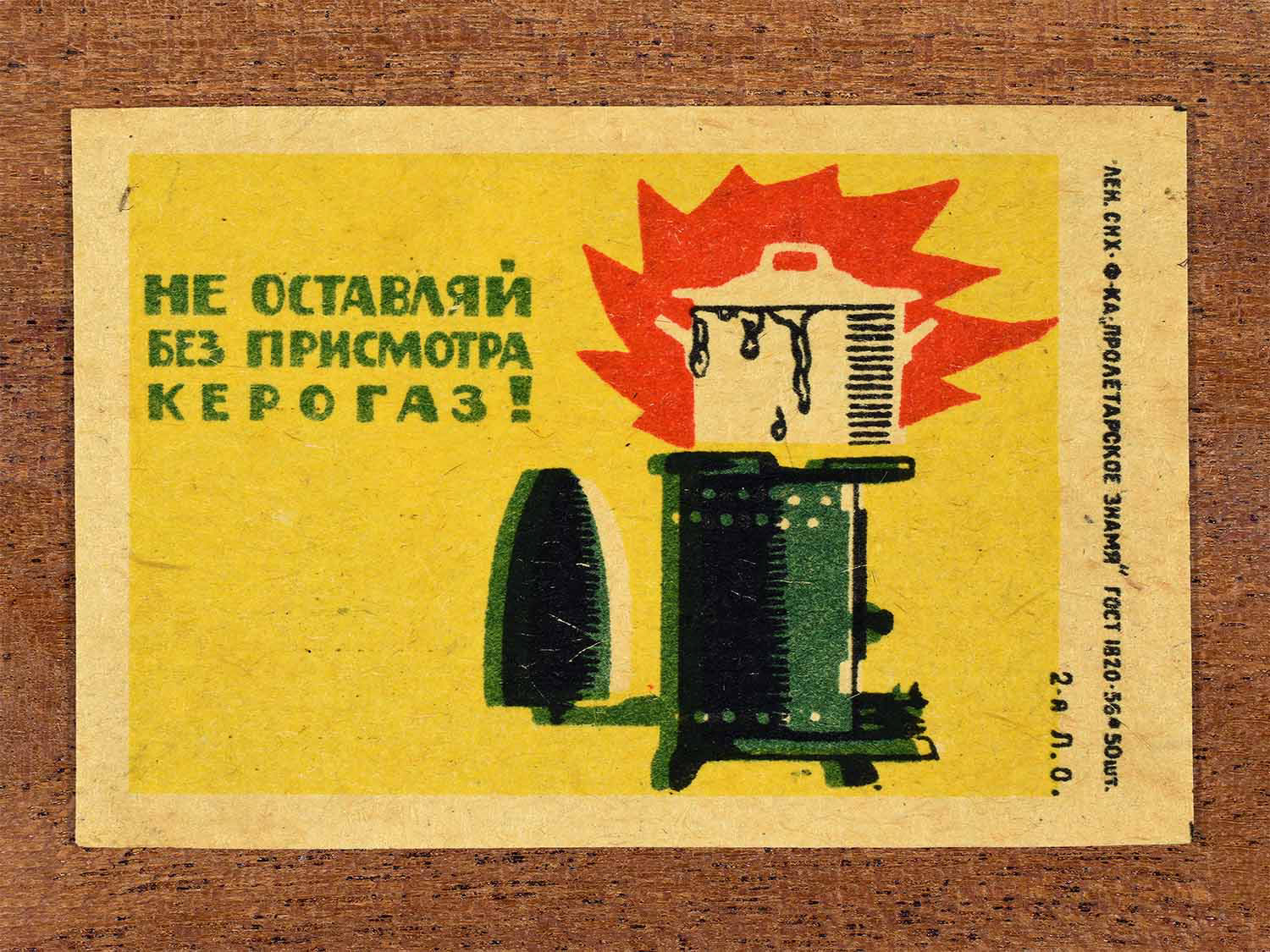 Vintage 1962 Soviet matchbox label showing a kerosene stove left unattended catching fire. In yellow, red, green and black colours. Produced by the Proletarian Banner match factory to promote safe use of domestic heating devices.