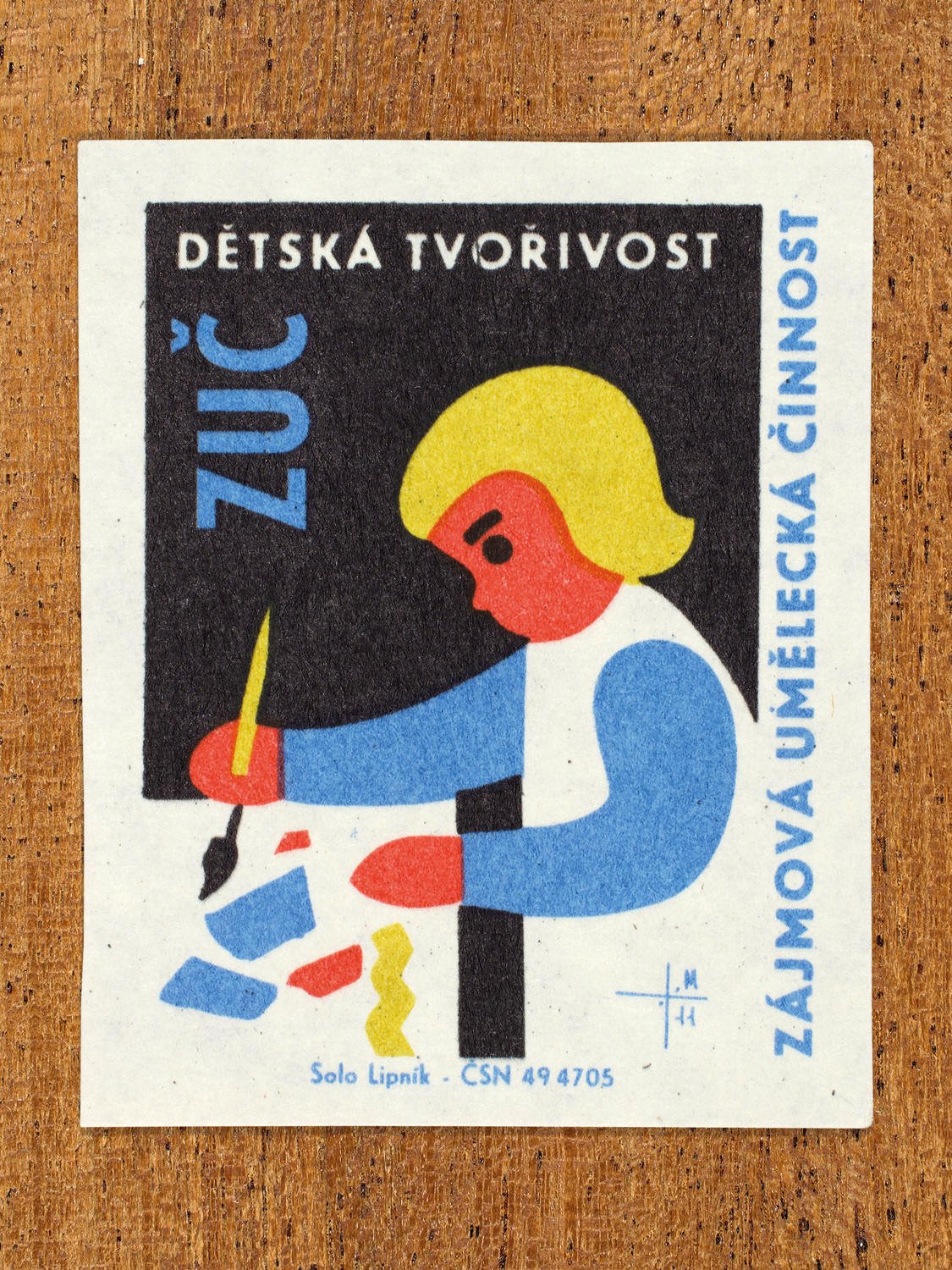 Vintage 1969 Czech matchbox label showing a stylised child sat at a table and painting, in blue, yellow and black colours. Produced by the Solo Lipník match factory to promote state-organised art groups in Czechoslovakia.