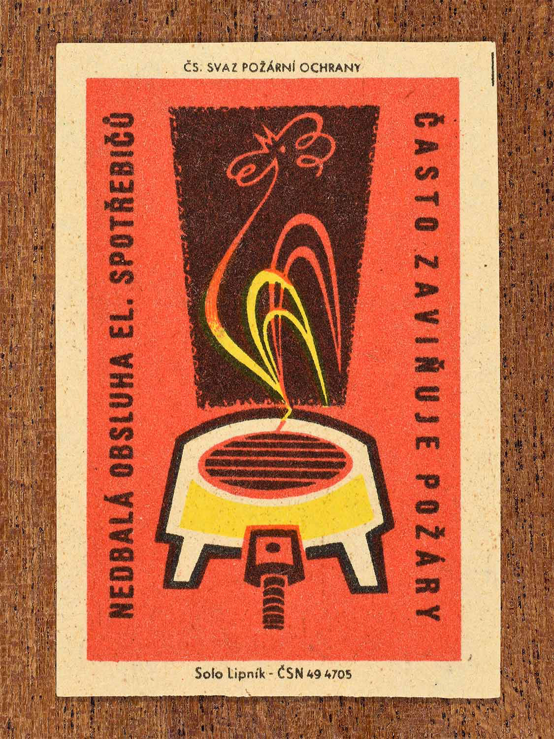Vintage c. 1961 Czech matchbox label showing an electric hotplate with flames forming a rooster in red, yellow, and black colours. Produced by the Solo Lipník match factory to warn that careless use of electrical appliances often causes fires.