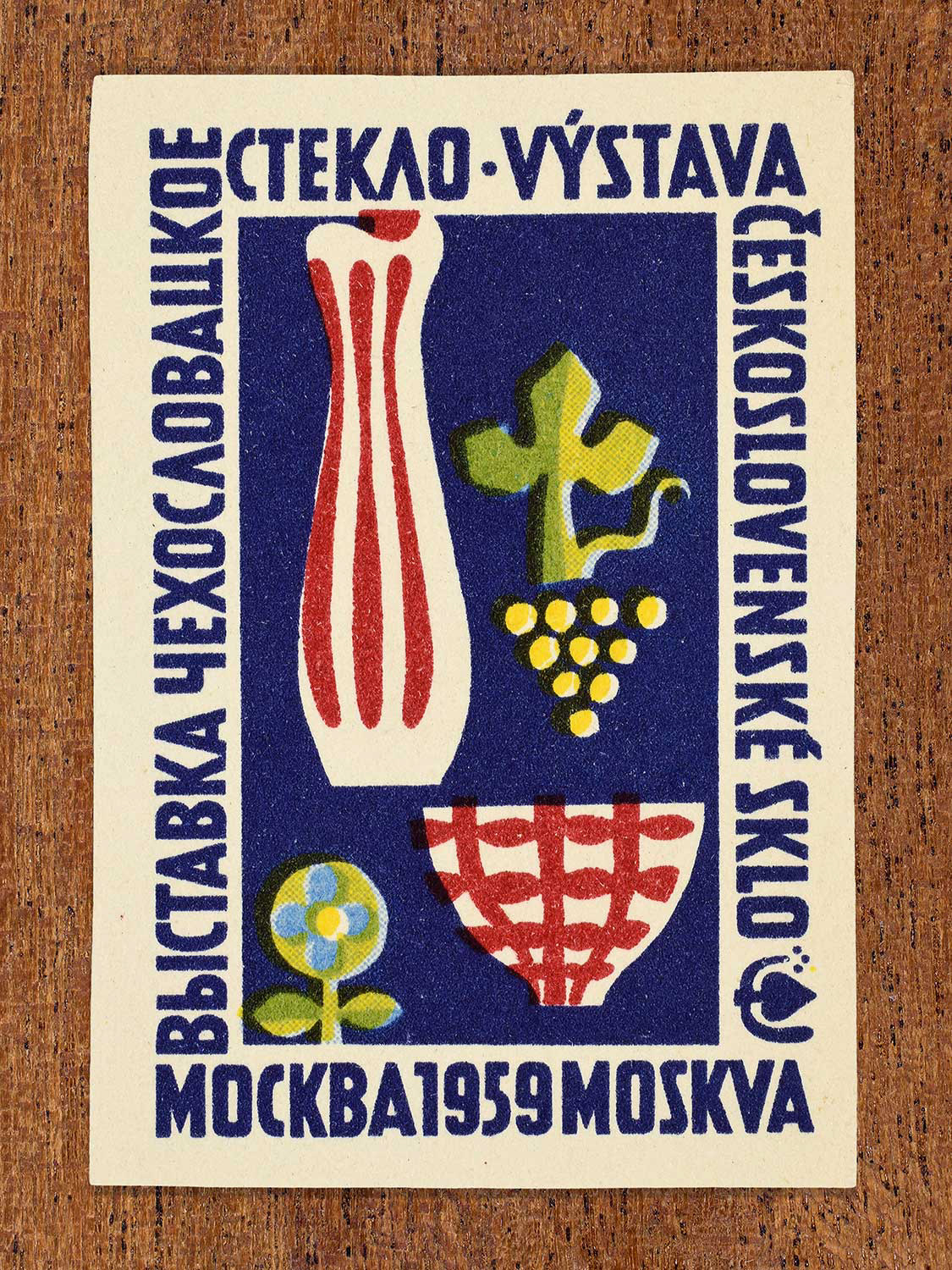 An illustration of two stylised glass vessels on a blue background depicted on a 1959 vintage matchbox label. The design functions to promote an international glass exhibition in Moscow.