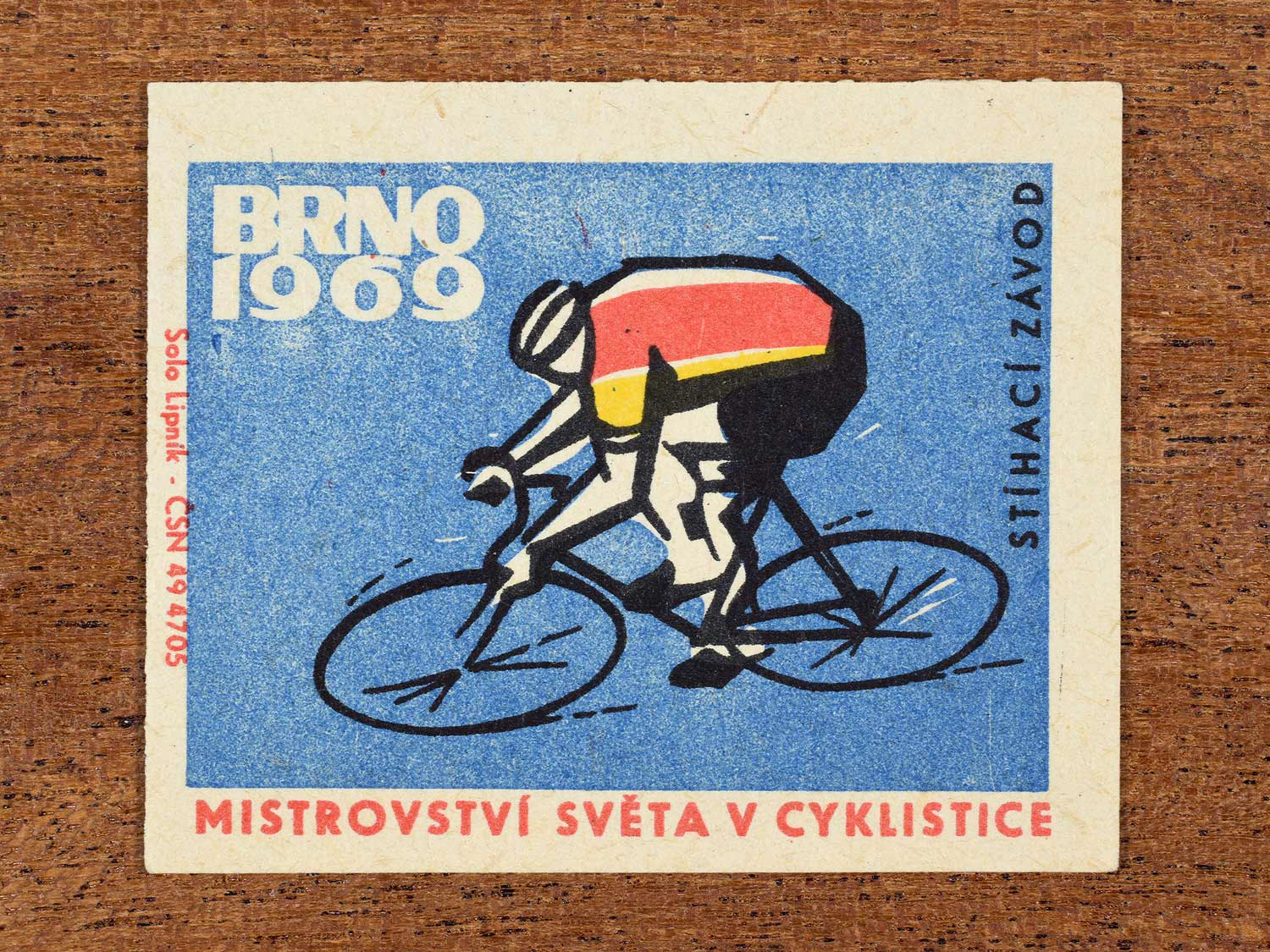 Vintage 1969 Czech matchbox label showing a stylised single cyclist in a road race posture, on a blue background. Produced by the Solo Lipník match factory to promote road racing at a cycling championship in Brno, Czechoslovakia.