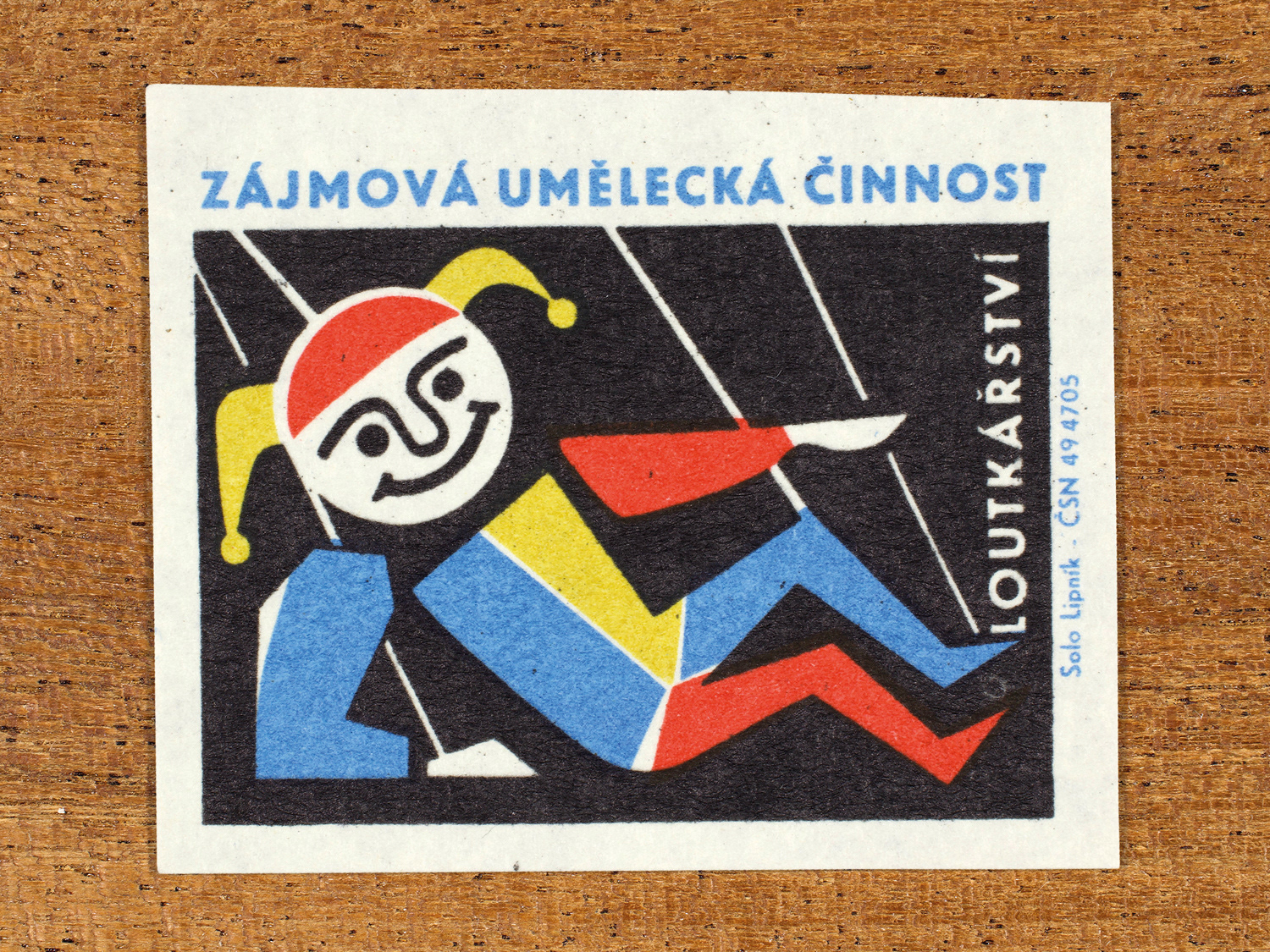 Vintage 1969 Czech matchbox label showing a stylised jester puppet laying on the floor, in blue, red, yellow and black colours. Produced by the Solo Lipník match factory to promote state-organised art groups in Czechoslovakia.