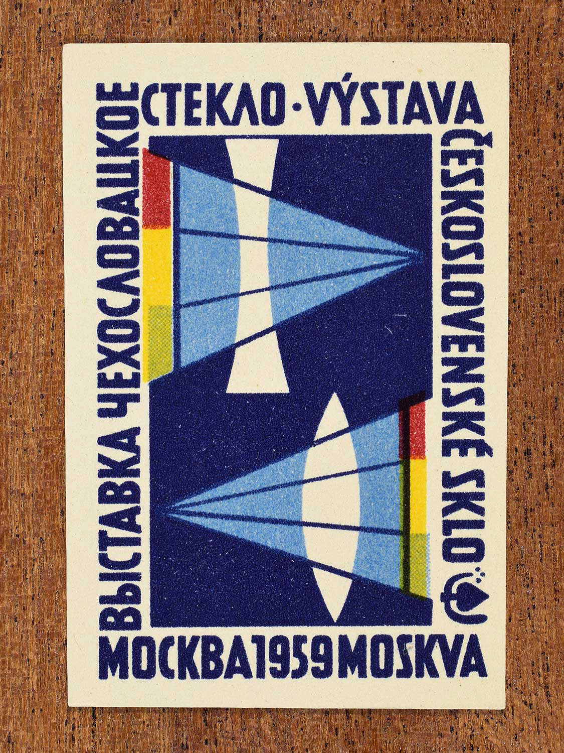Vintage 1959 Czechoslovak matchbox label showing two stylised yellow, blue, and red abstract glass sculptures against a dark blue background, produced by an unknown factory to promote Czechoslovak glass design at an international exhibition in Moscow.