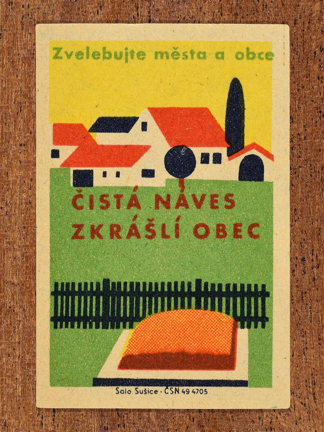Vintage 1961 Czech matchbox label showing a stylised graphic of houses, trees, a wooden fence, and a clean village green. Produced by the Solo Sušice match factory to promote clean, beautiful village squares.