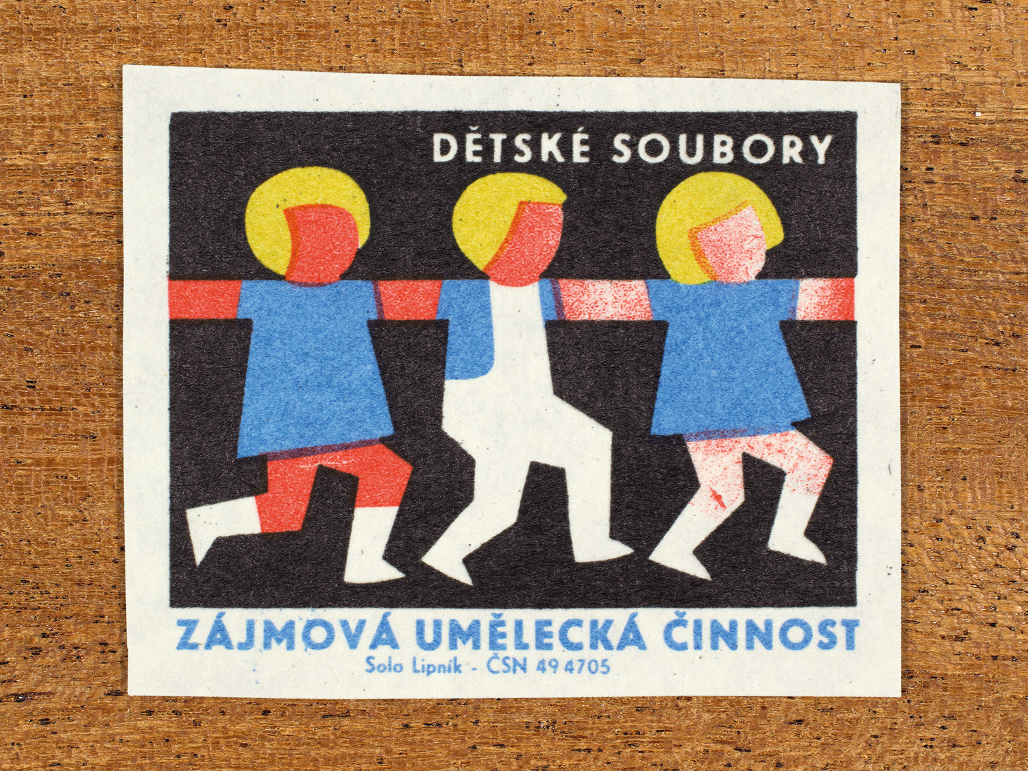 Vintage 1969 Czech matchbox label showing three stylised child figures moving together with linked arms, in blue, red, yellow and black colours. Produced by the Solo Lipník match factory to promote state-organised art groups in Czechoslovakia.