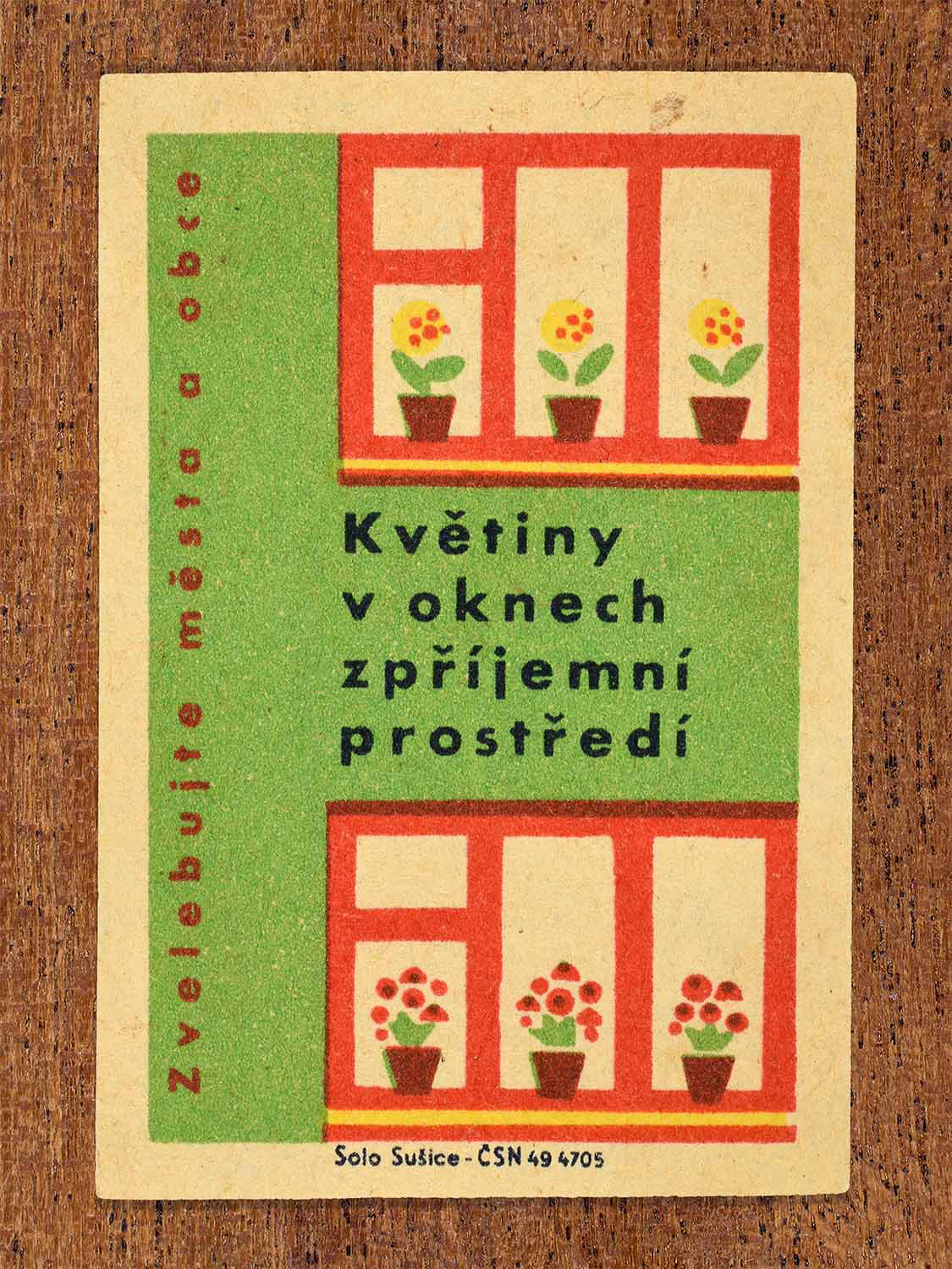 Vintage 1961 Czech matchbox label showing stylised window frames filled with small potted flowers on red window sills, on a green background. Produced by the Solo Sušice match factory to encourage residents to place flowers in windows to beautify urban environments.