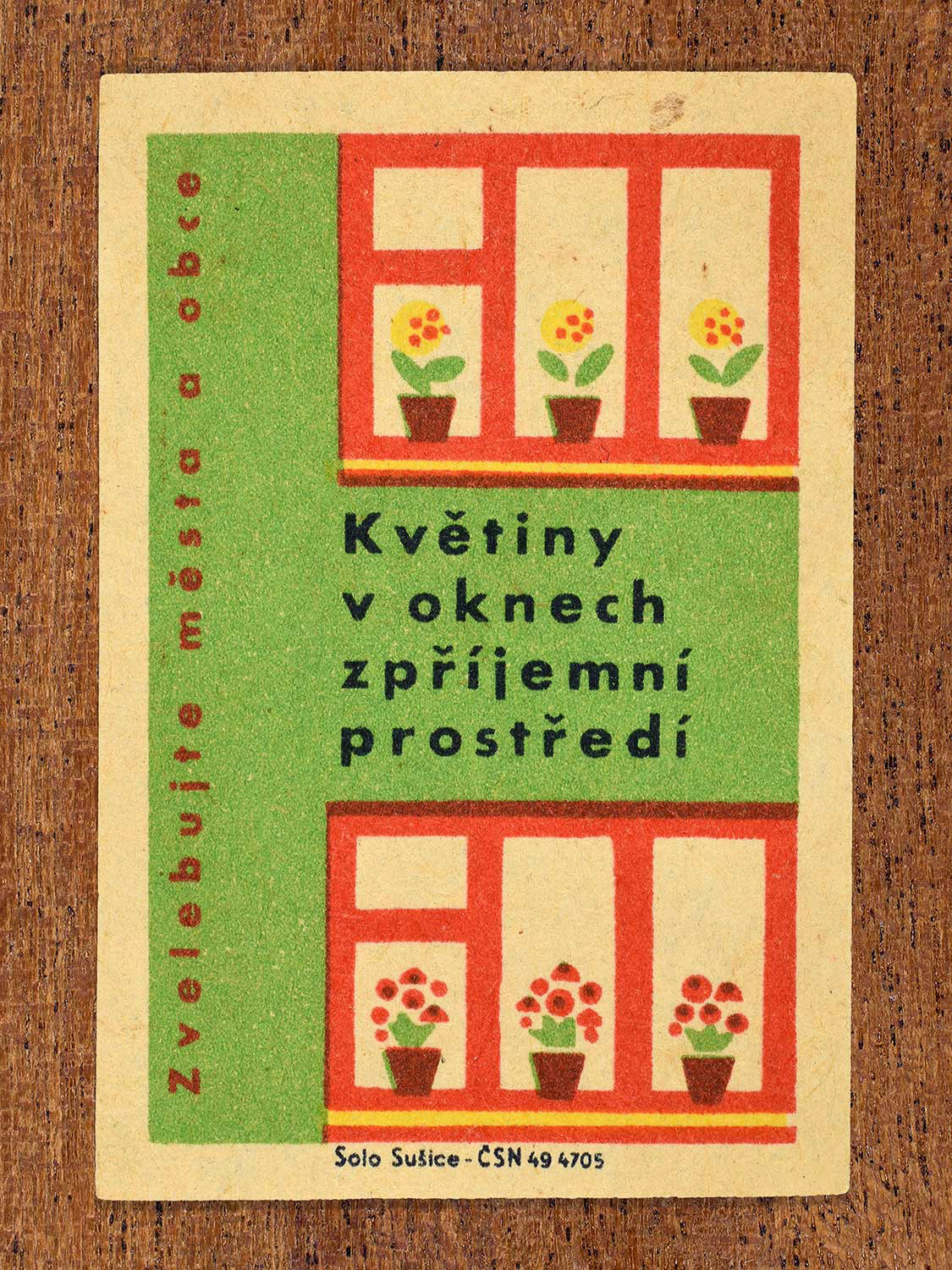 Vintage 1961 Czech matchbox label showing stylised window frames filled with small potted flowers on red window sills, on a green background. Produced by the Solo Sušice match factory to encourage residents to place flowers in windows to beautify urban environments.