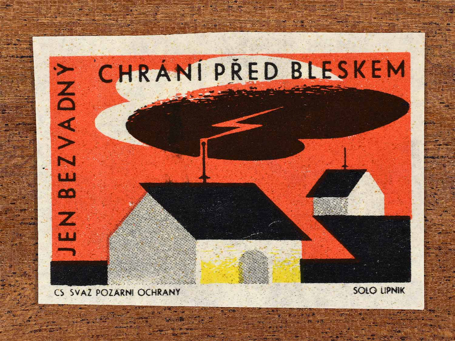 Vintage 1963 Czech matchbox label showing a lightning strike hitting a building in red, black and yellow colours. Produced by the Solo Lipník match factory to promote proper lightning protection systems.