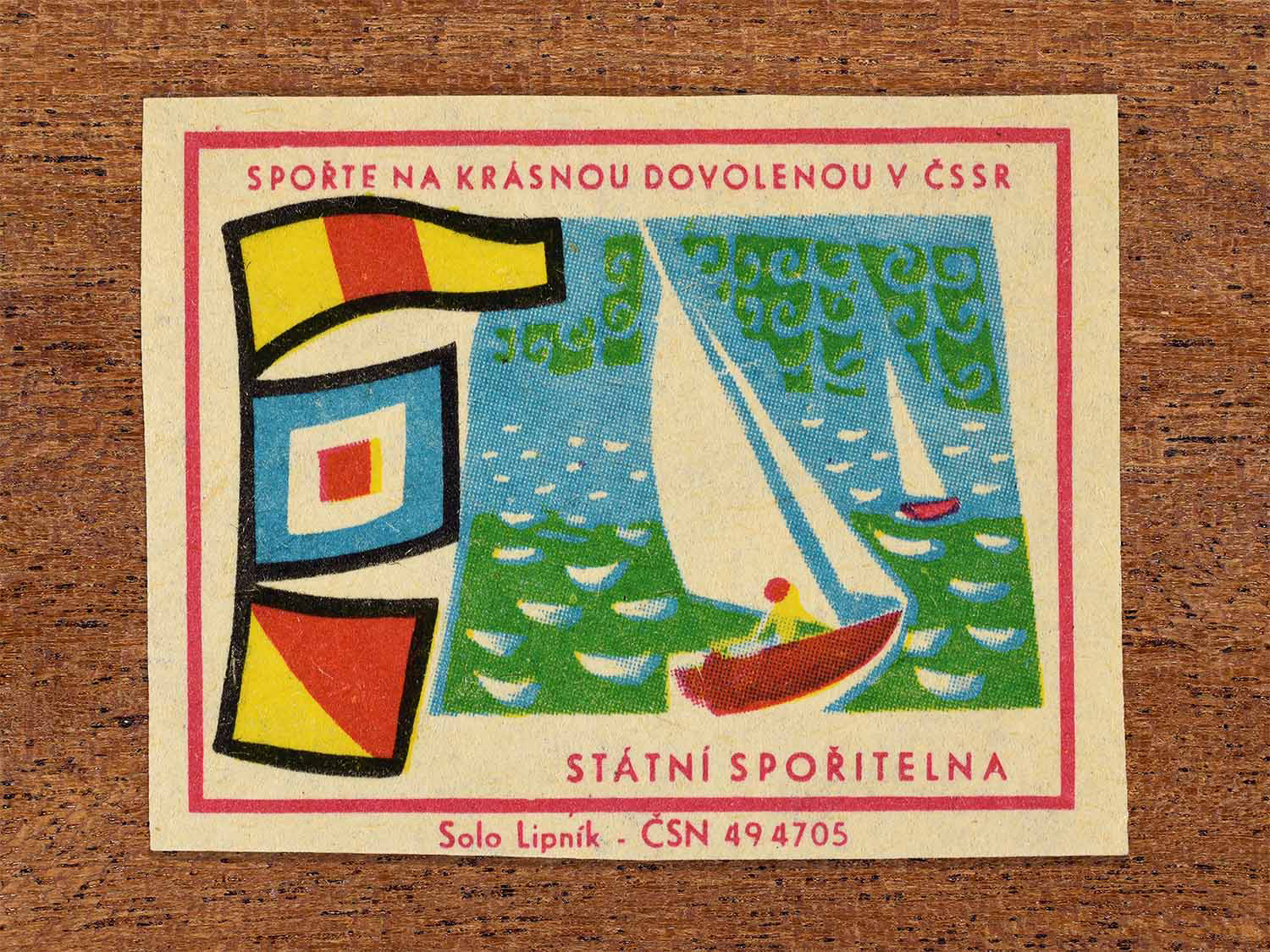 Vintage 1968 Czech matchbox label showing a sailboat on a lake. Produced by the Solo Lipník match factory to promote saving money for holidays in the Czechoslovak Socialist Republic.