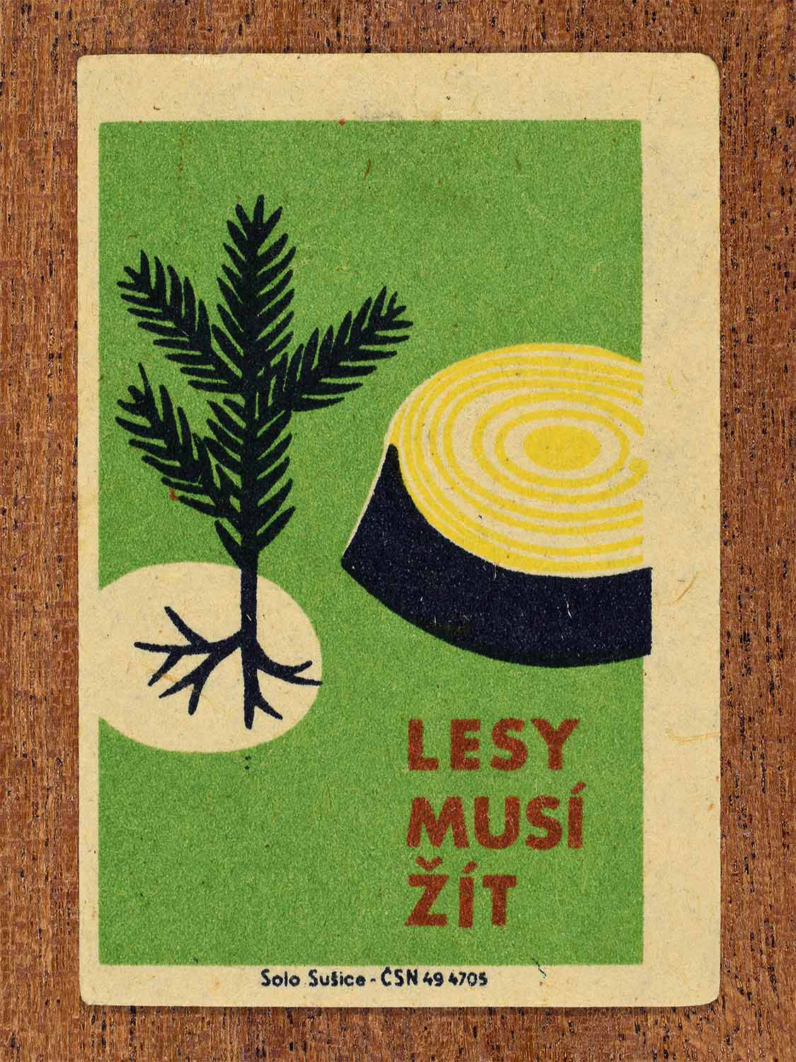 Vintage 1961Czech matchbox label showing a rooted plant and a cross-section of a cut tree trunk on a green background. Produced by the Solo Sušice match factory to promote forest preservation and ecological health.