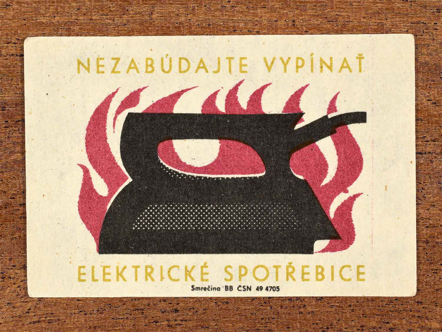 Vintage 1964 Czechoslovak matchbox label showing a stylised electric iron with flames behind it, in black, yellow and red. Produced by the Smrečina match factory to remind people to switch off electrical appliances.